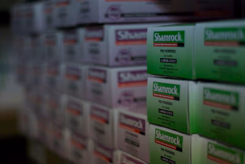 Stacks of Shamrock-branded boxes on shelves inside a dim storage room at KKMS diaper service.