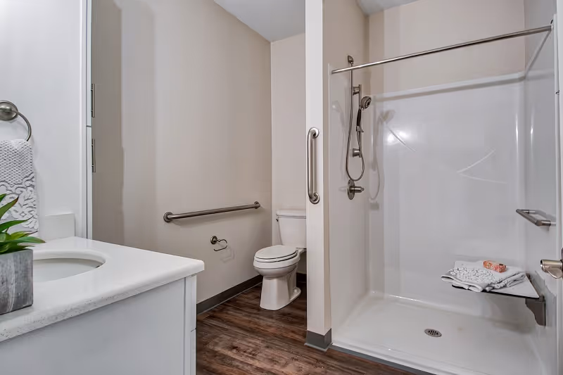 Accessible bathroom featuring a walk-in shower, toilet, sink, and grab bars.
