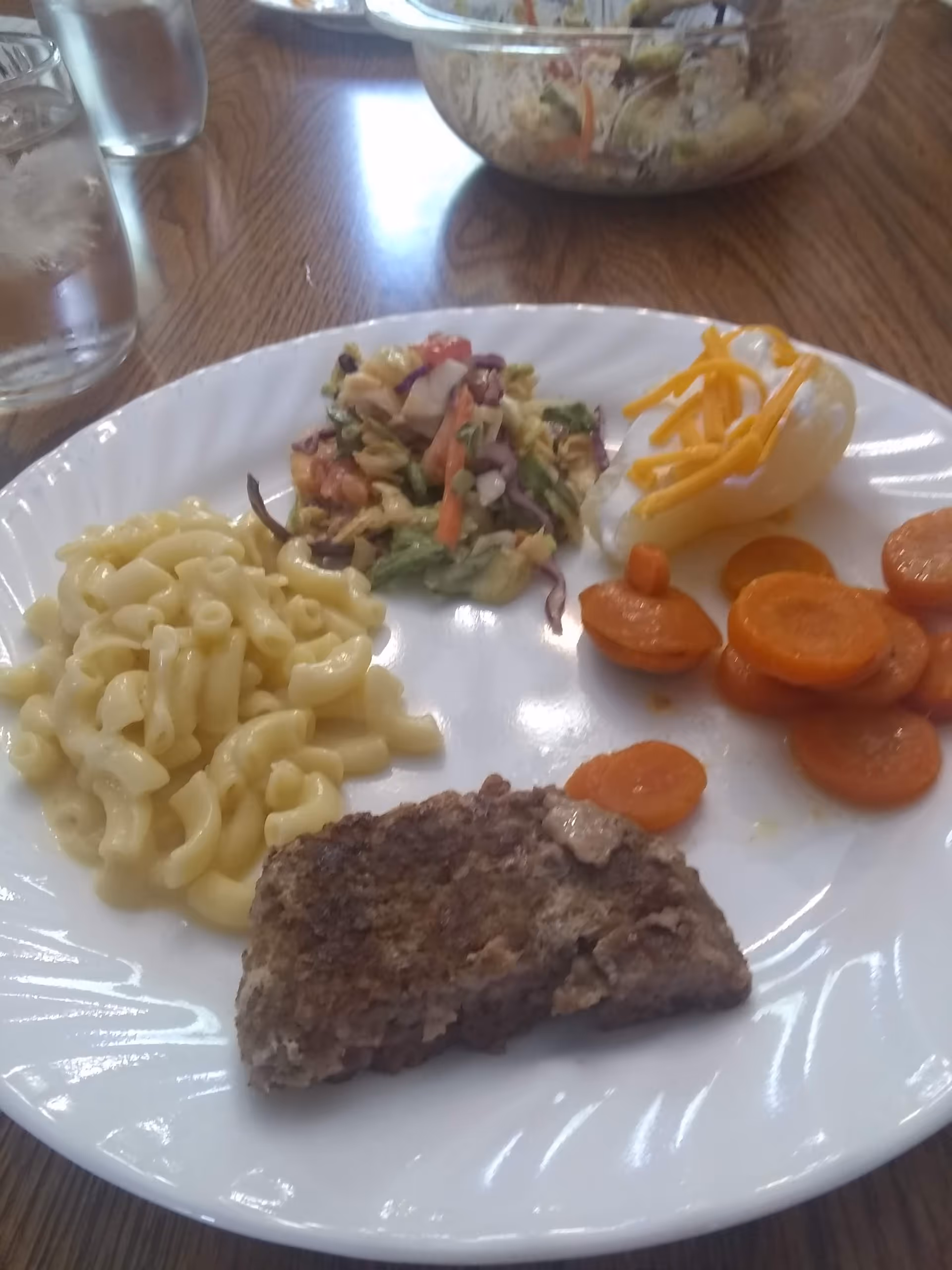 A plated meal showing pasta, mixed salad, sliced carrots, and a breaded meat patty.