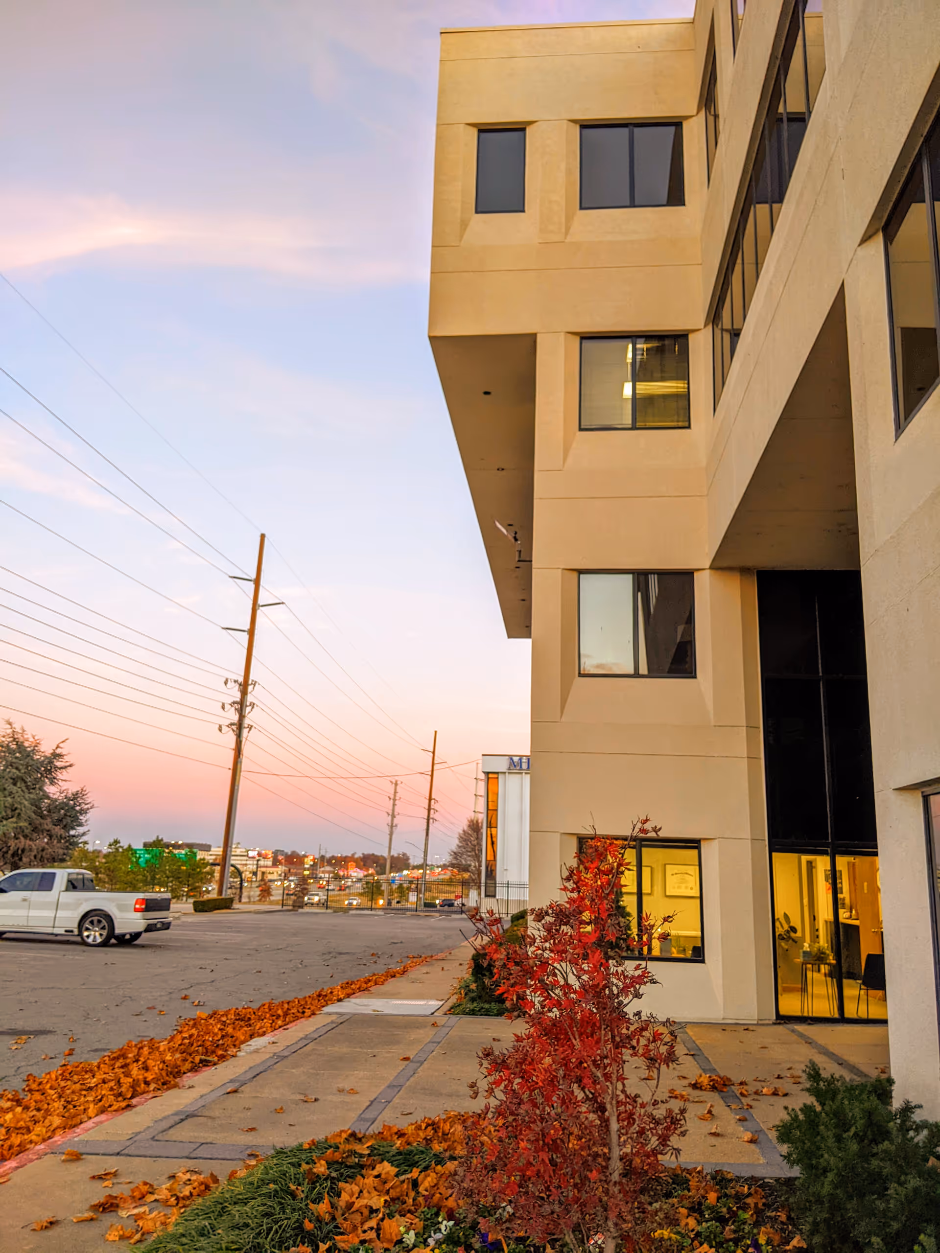 Exterior view of a modern building entrance with autumn landscaping and a parking lot.
