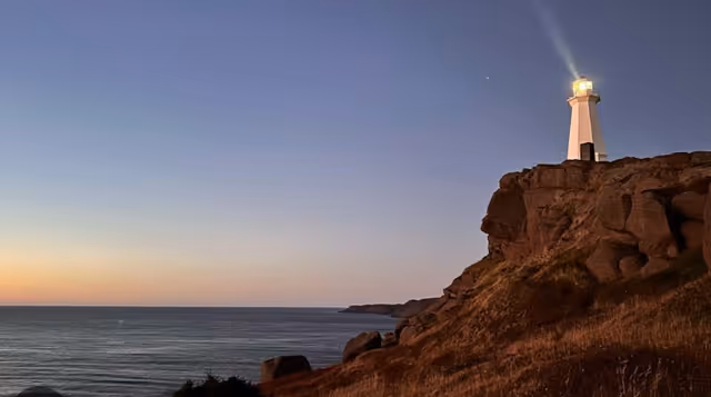Sunset over a rocky coastline with a lighthouse atop a cliff.