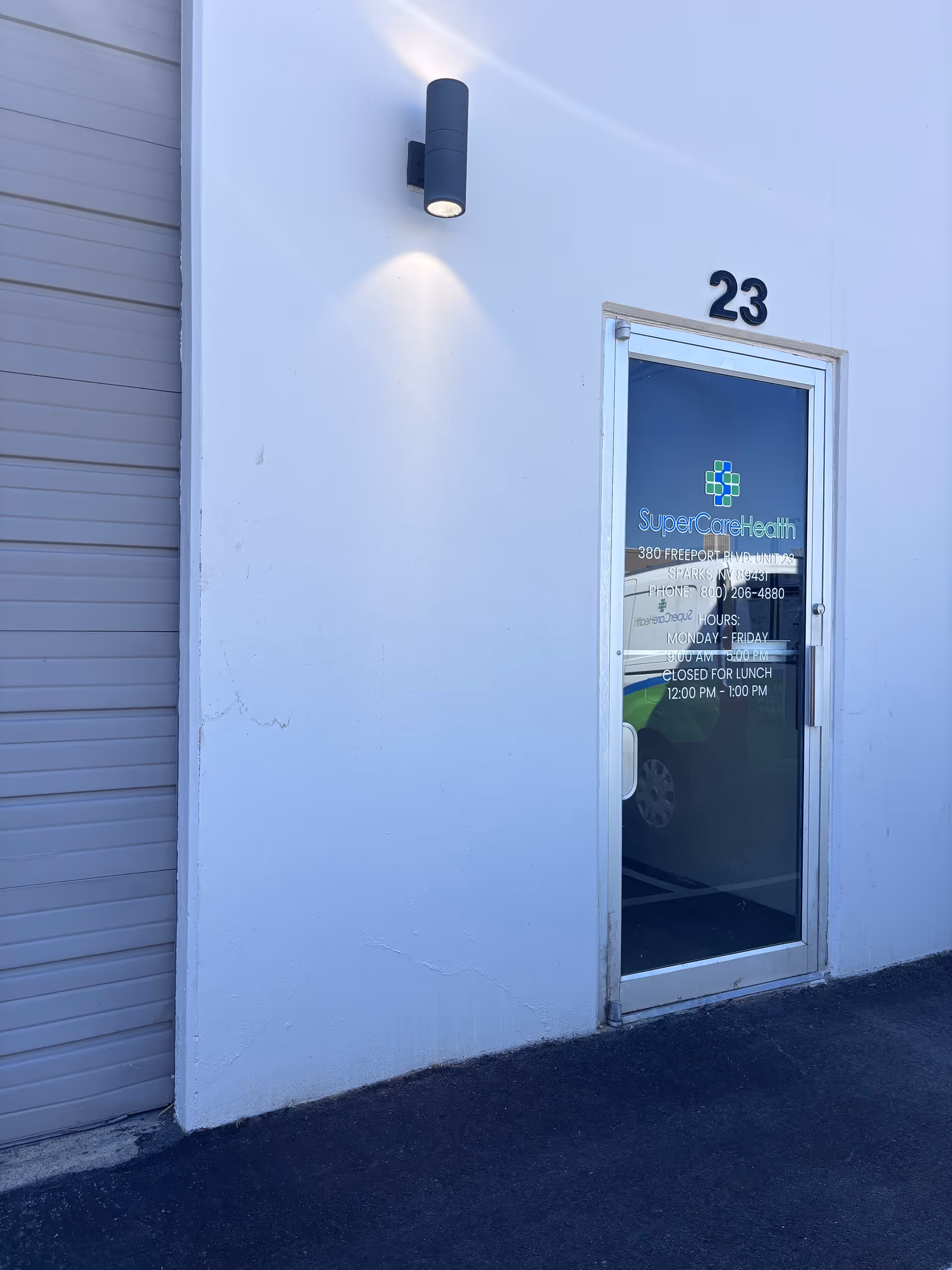 Exterior view of a white wall with a glass door labeled 23 and SuperCare Health signage.