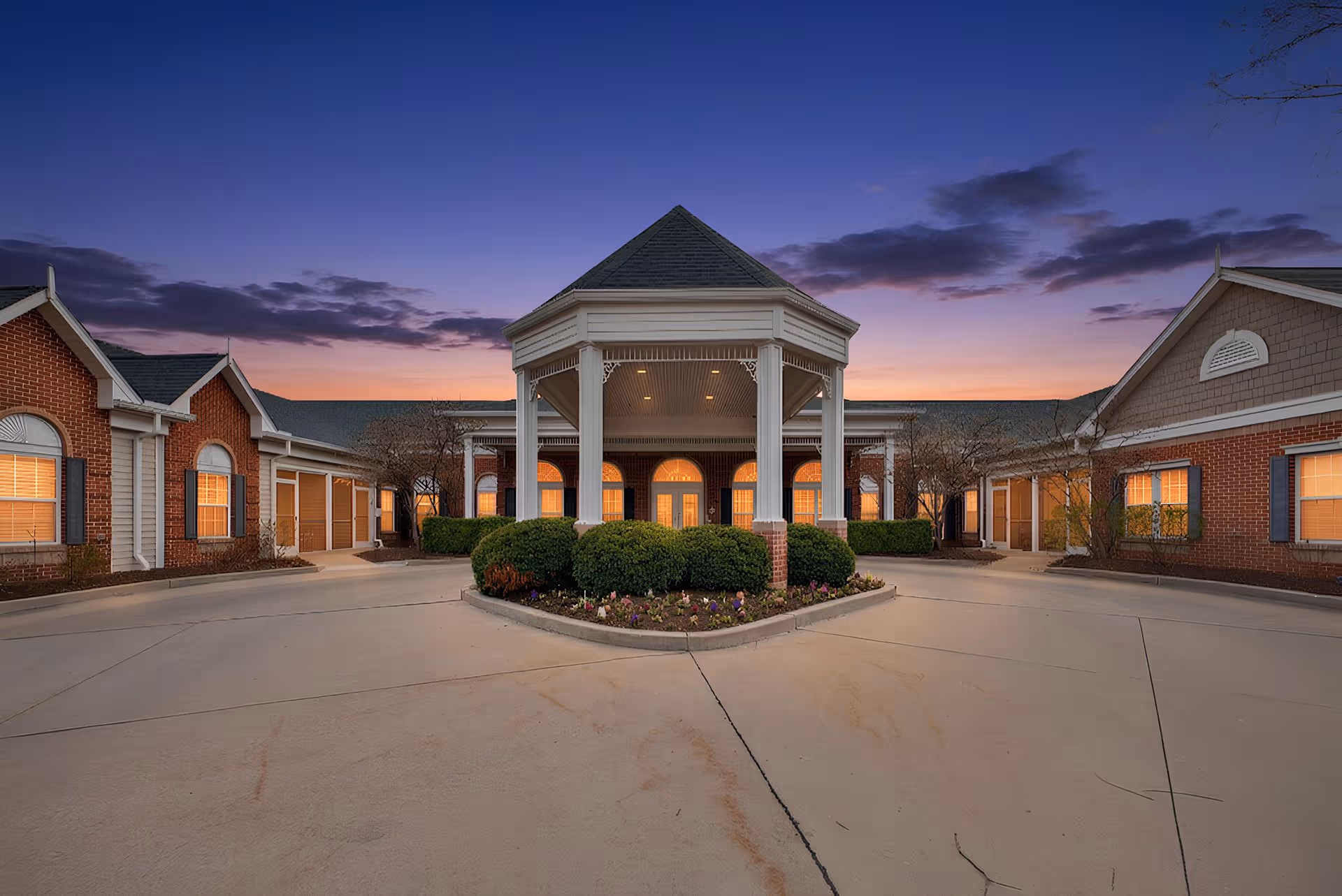 Sunset-lit senior living campus with brick buildings surrounding a central covered entrance portico.
