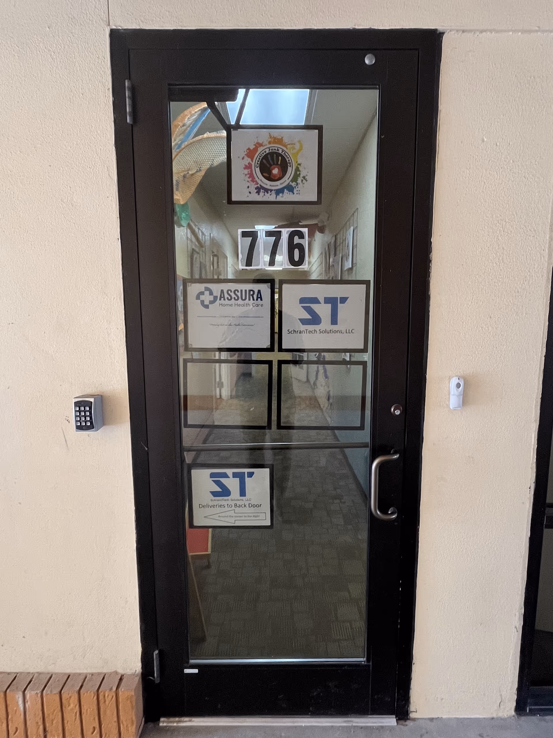 Black-framed glass door with logos and a hallway visible behind.