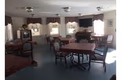 A shared dining room with several tables, chairs, curtains, and a TV on the wall.