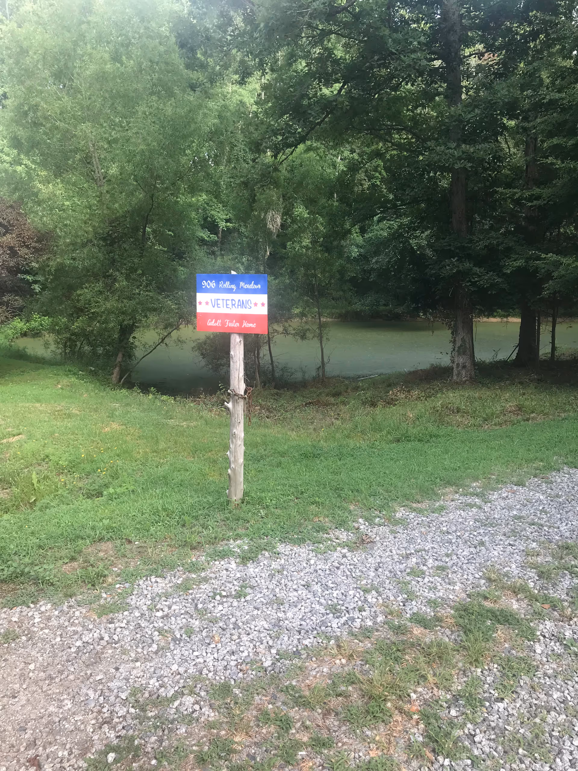 Outdoor scene with a wooden post sign near a pond, surrounded by trees.