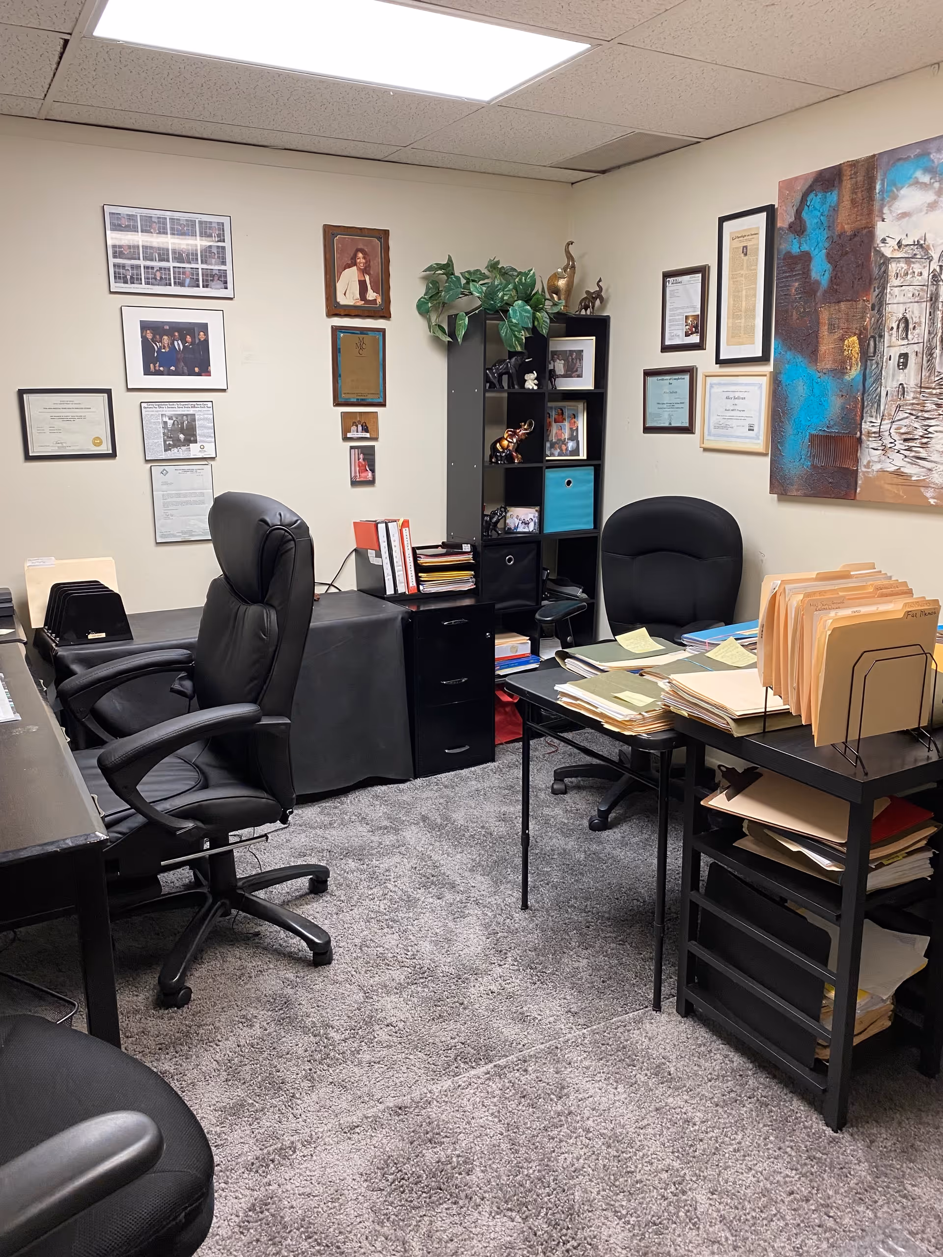 Office workspace with chairs, desks, files, and wall certificates in a facility.