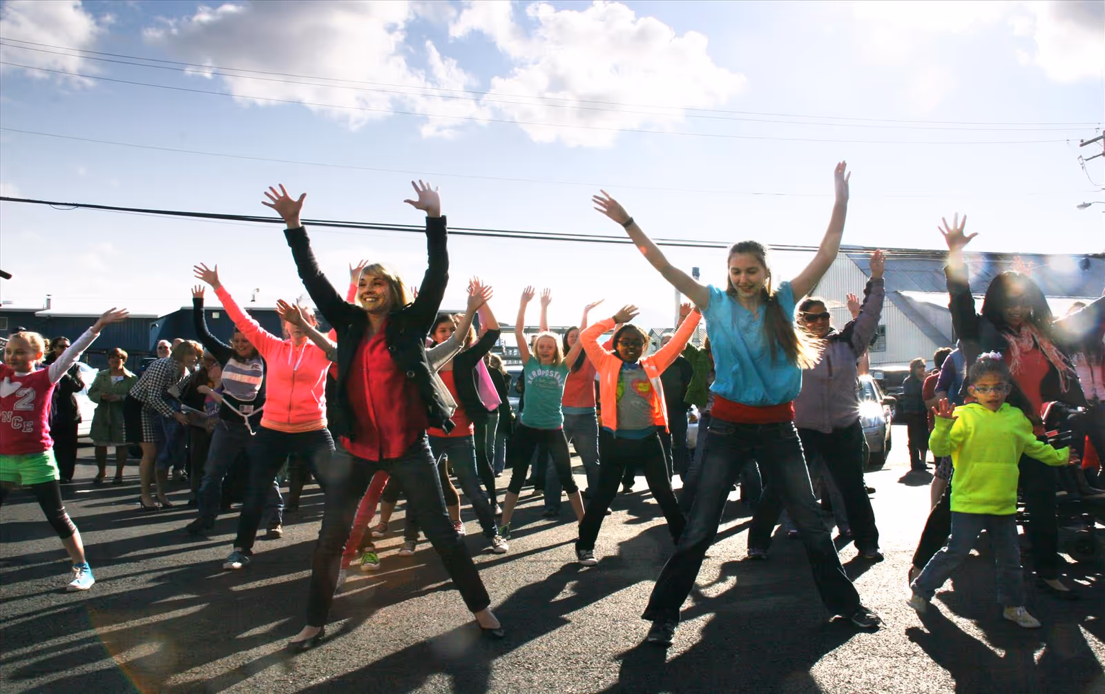 Group of people, including adults and children, exercise outdoors in a parking lot.