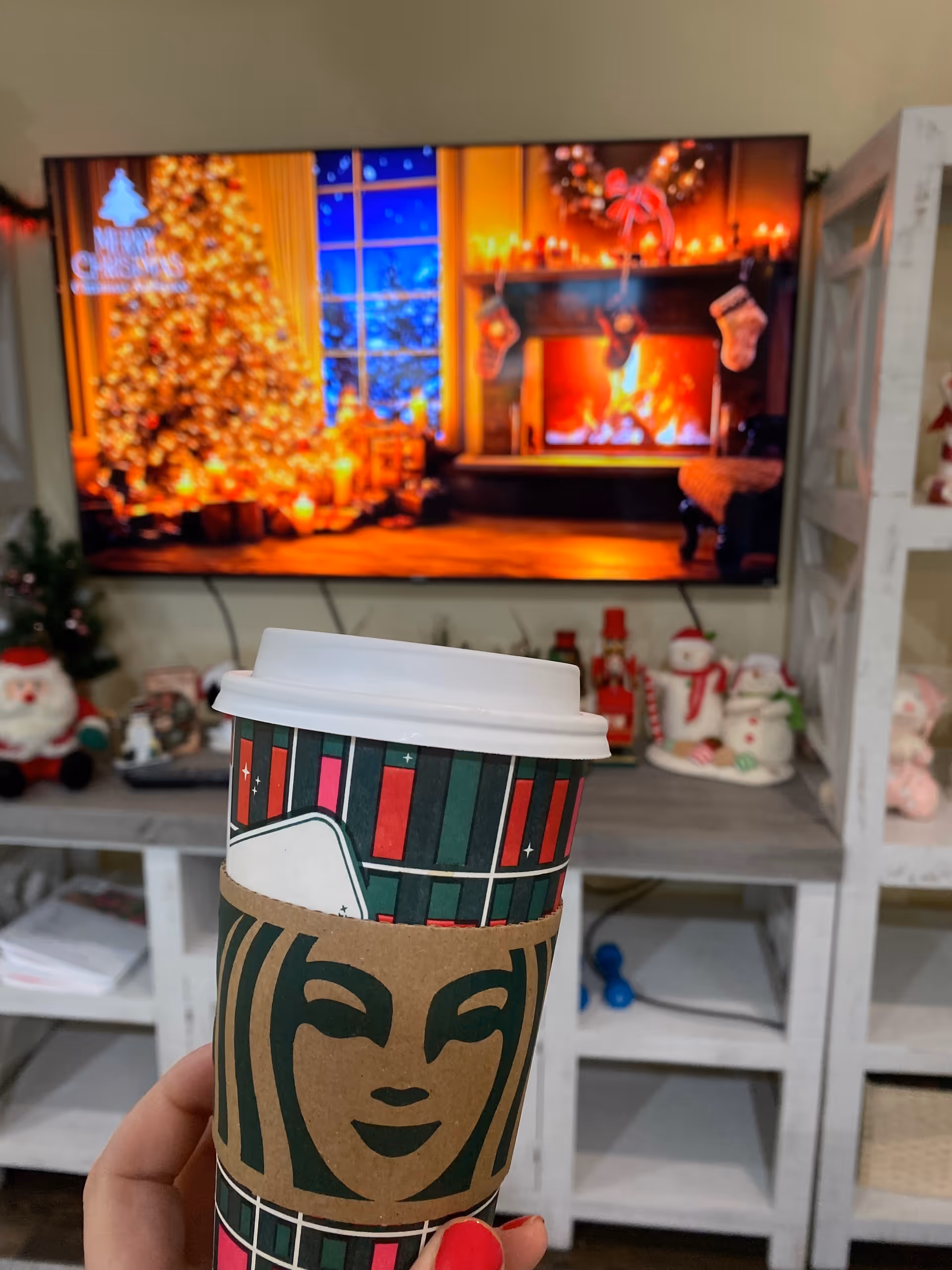 Hand holds a festive to-go cup in a Christmas-decorated living room.