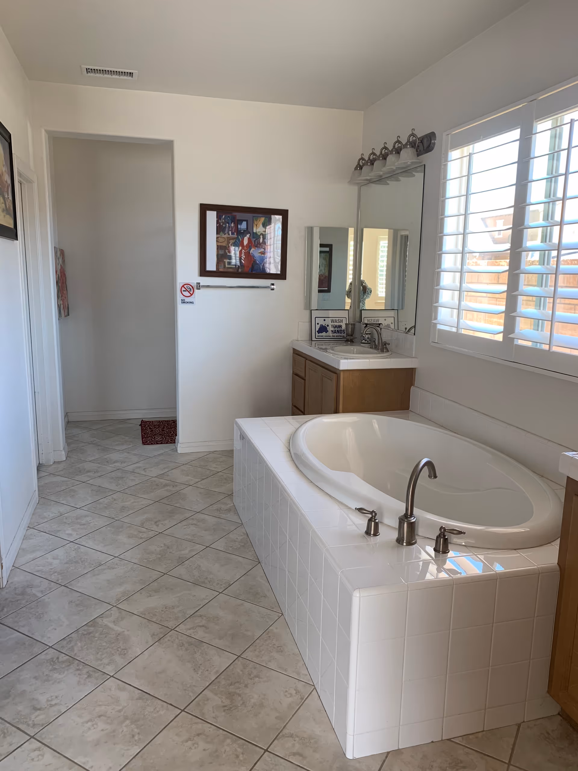 Bright bathroom featuring a large built-in tub, a sink, and window blinds.