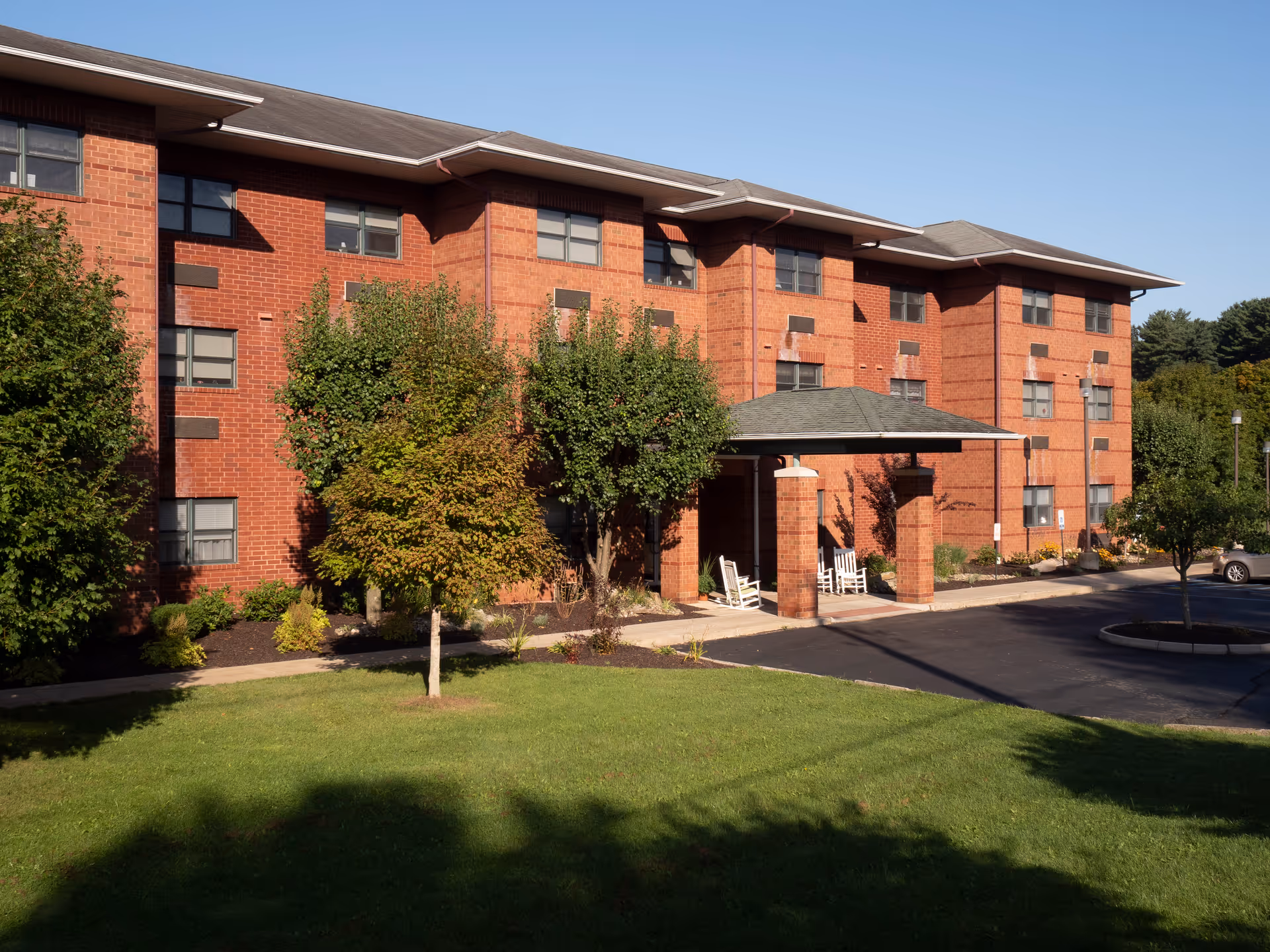 Red brick senior living building with a covered entrance and surrounding lawn.