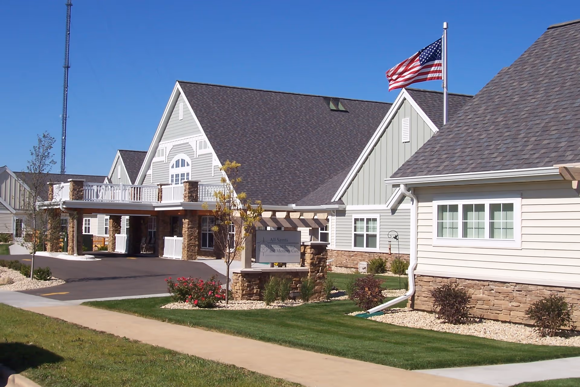 Front exterior of a memory care facility with a covered entrance, American flag, and landscaped lawn.
