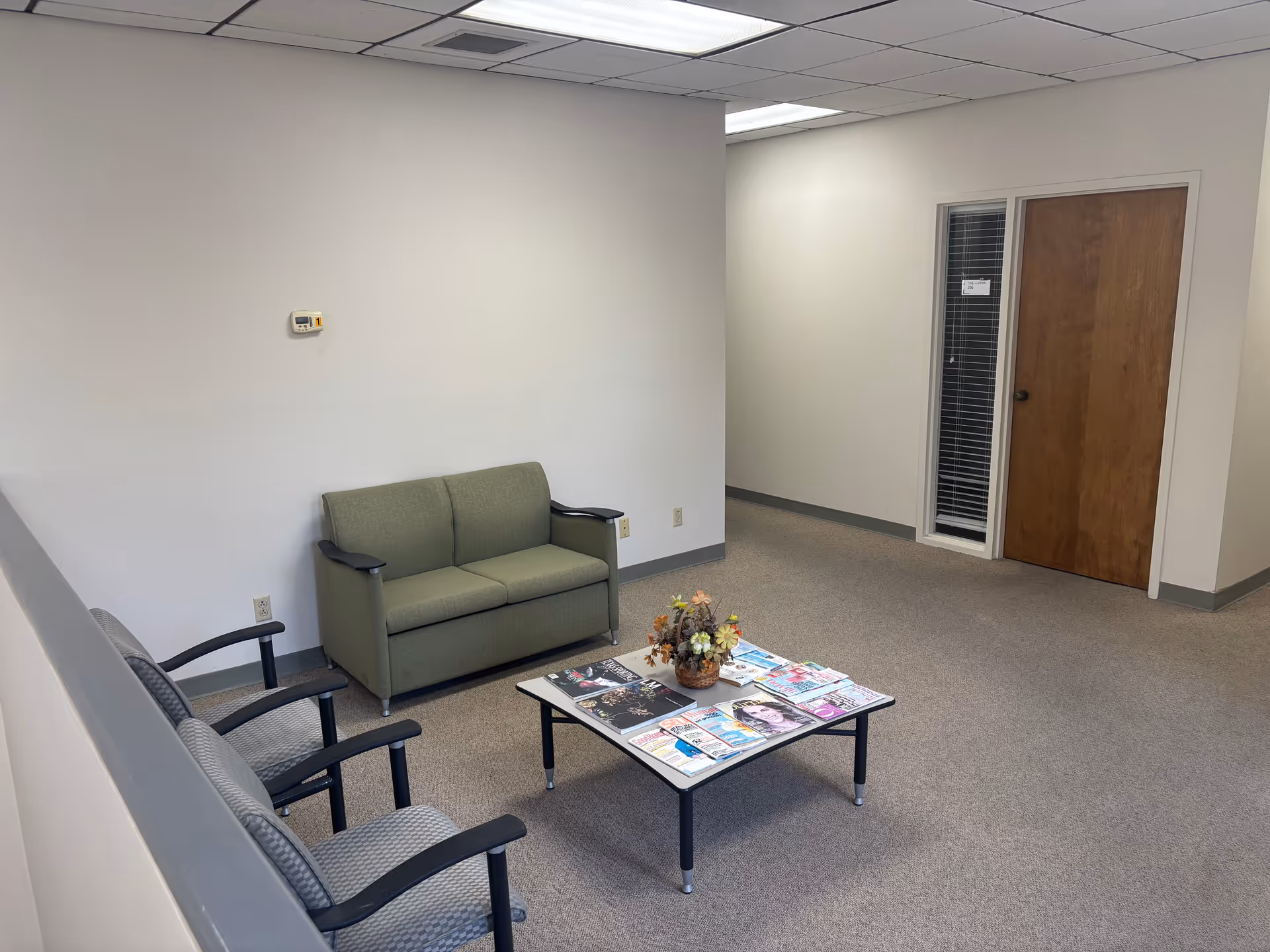 Waiting area with green loveseat, several chairs, and magazines on a coffee table.
