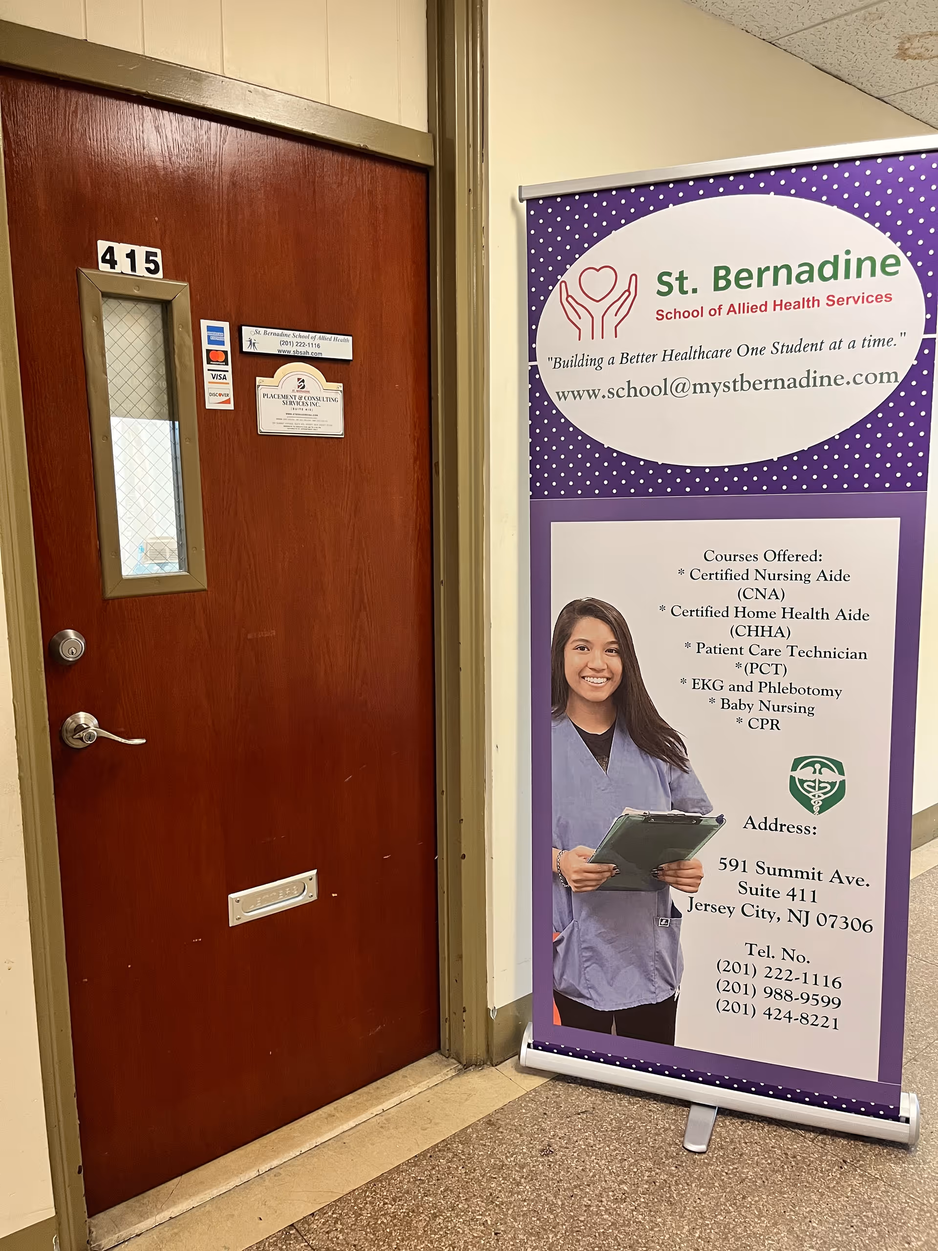 Interior hallway with a wooden door labeled 415 and a tall St. Bernadine banner.