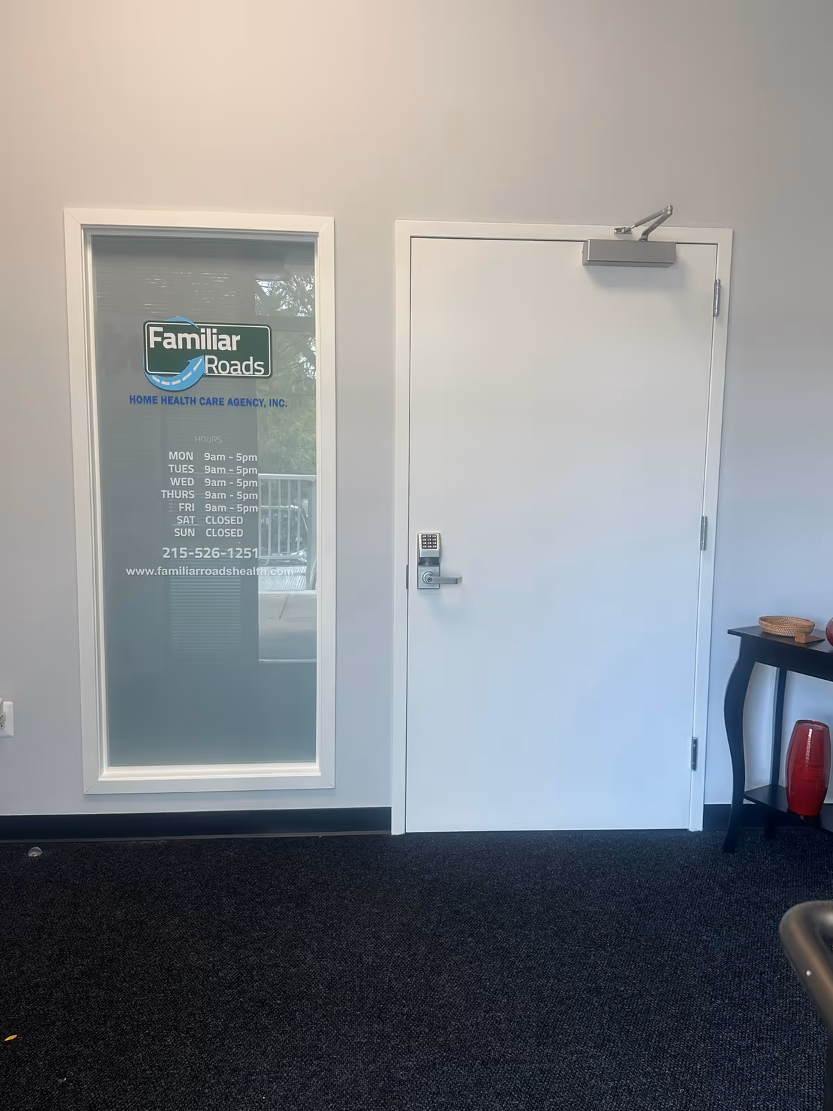 White interior door beside a glass panel with Familiar Roads logo and hours.