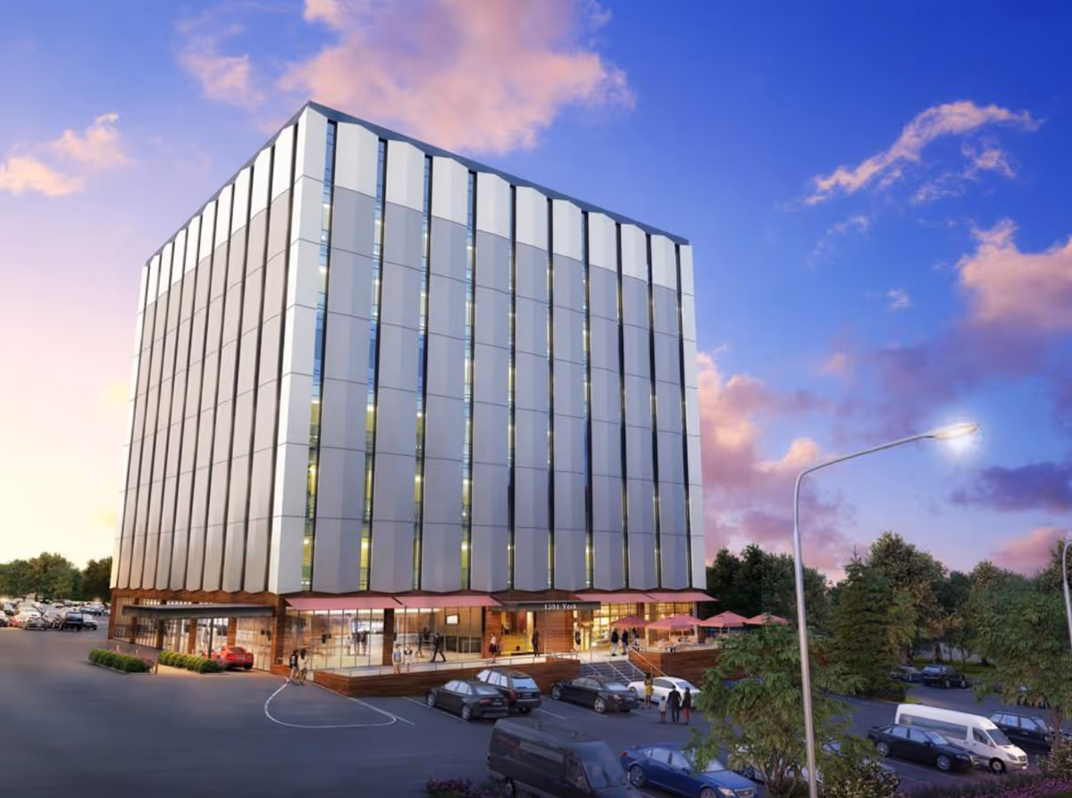 Tall glass-fronted senior living building with a parking lot at sunset.