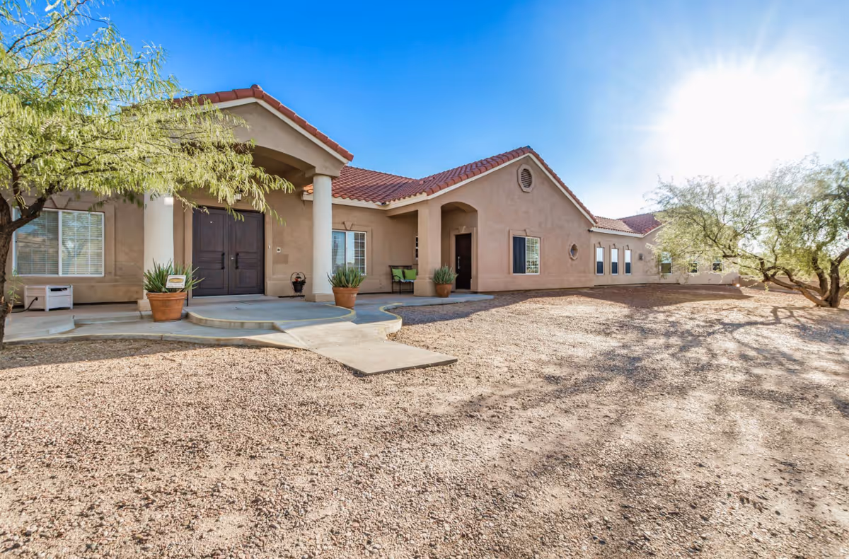 Single-story beige senior living facility with columns, a curved entrance, and gravel surroundings.
