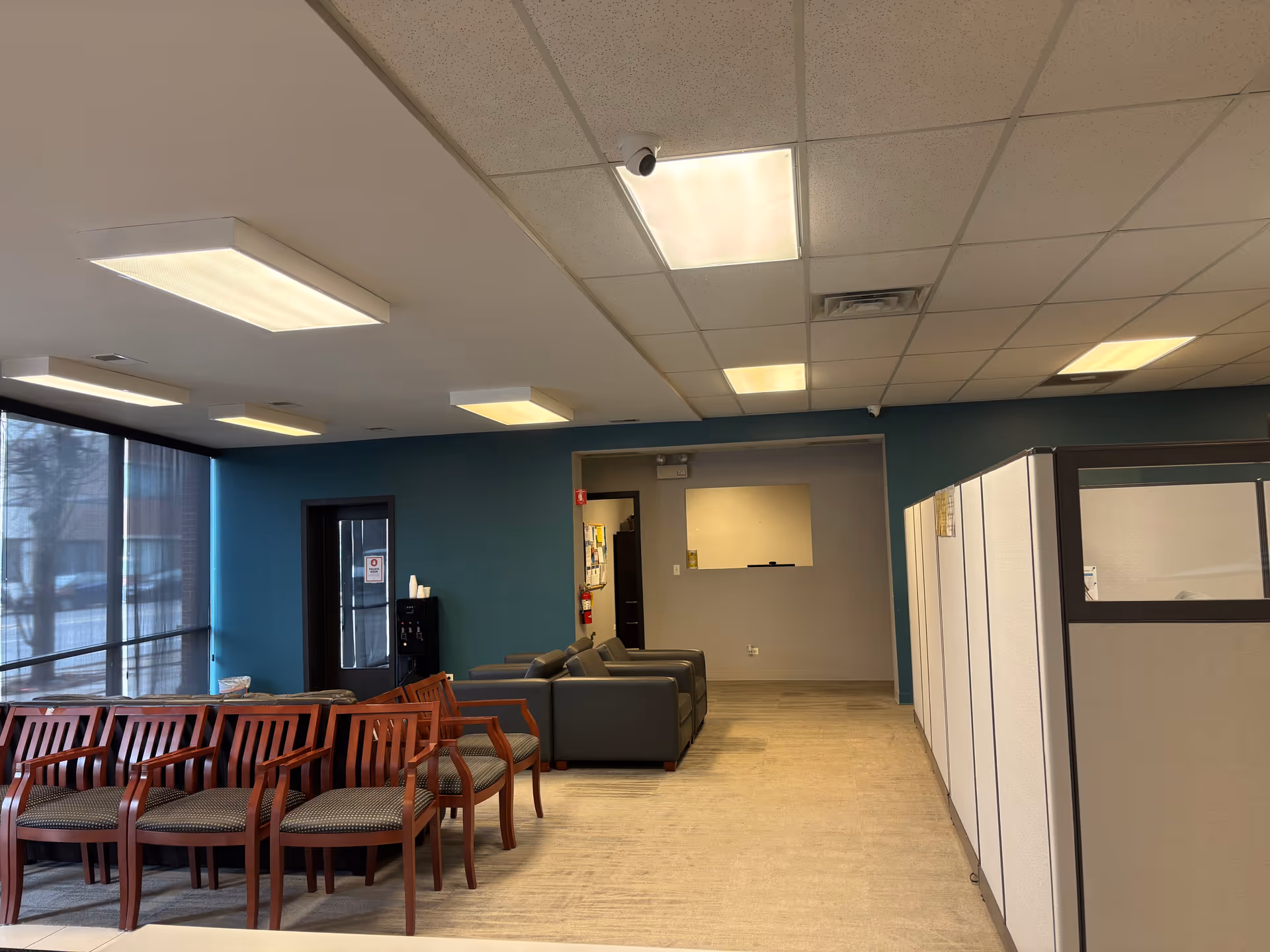 Indoor waiting area with teal wall, multiple wooden chairs and gray couches.