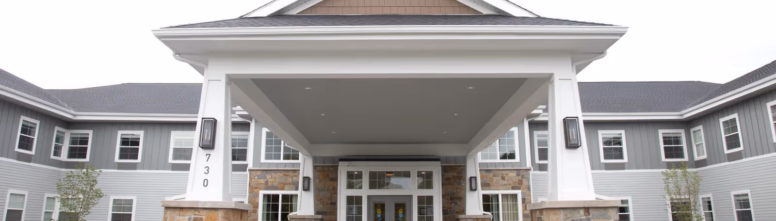 Front exterior view of Provision Living at Forest Hills building with a covered entrance supported by white columns and stone bases, multiple windows, and a gray roof.