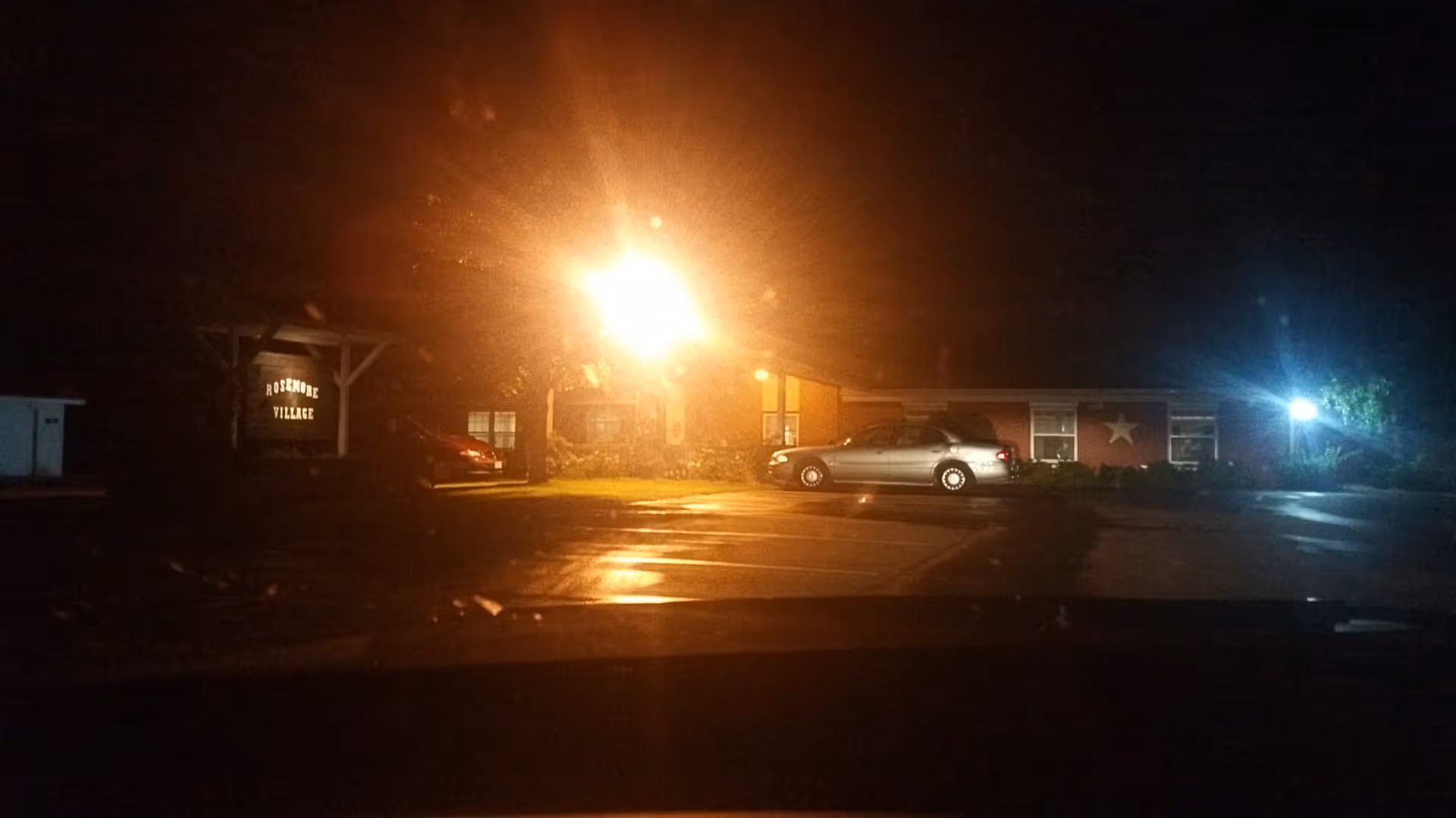 Night exterior view of Rosemore Village with a sign, parking lot, and illuminated entrance.