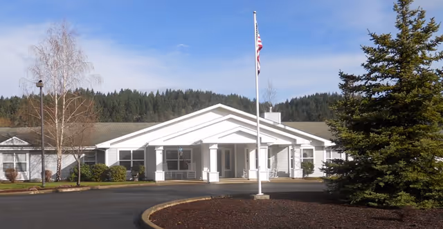 White senior living facility front entrance with flagpole and trees.