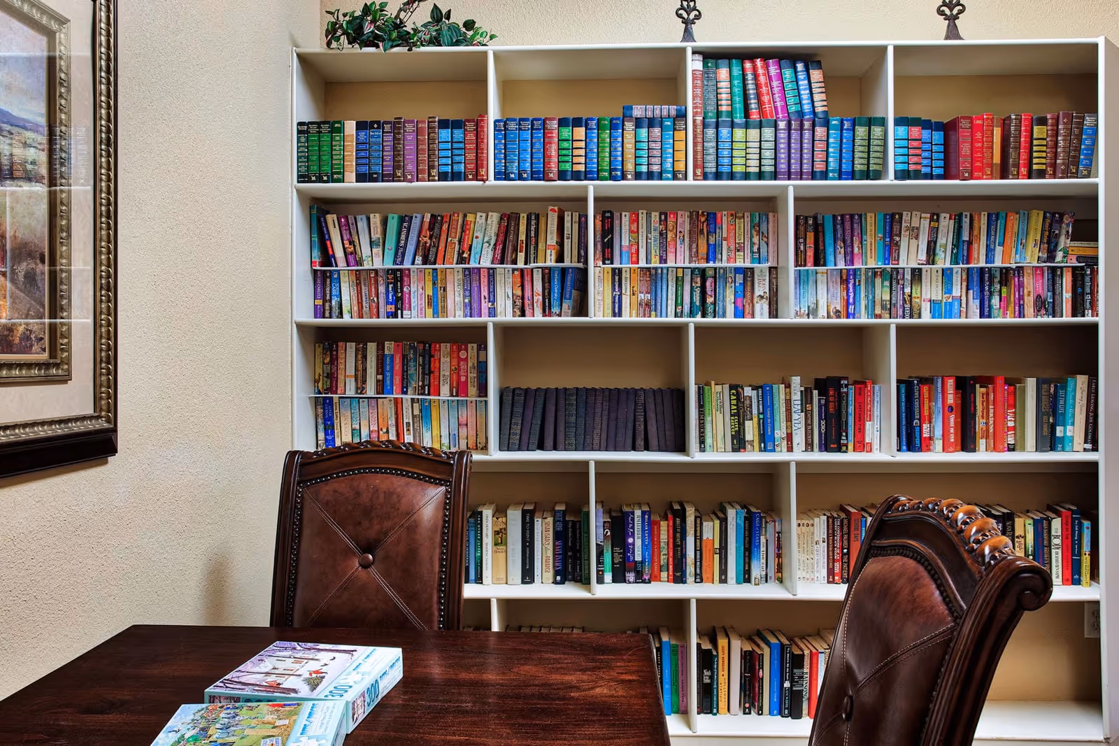 Wooden table and leather chairs in front of a large white bookshelf filled with books.