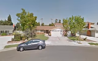 Exterior view of a single-story senior living building with a parked car and trees in front.