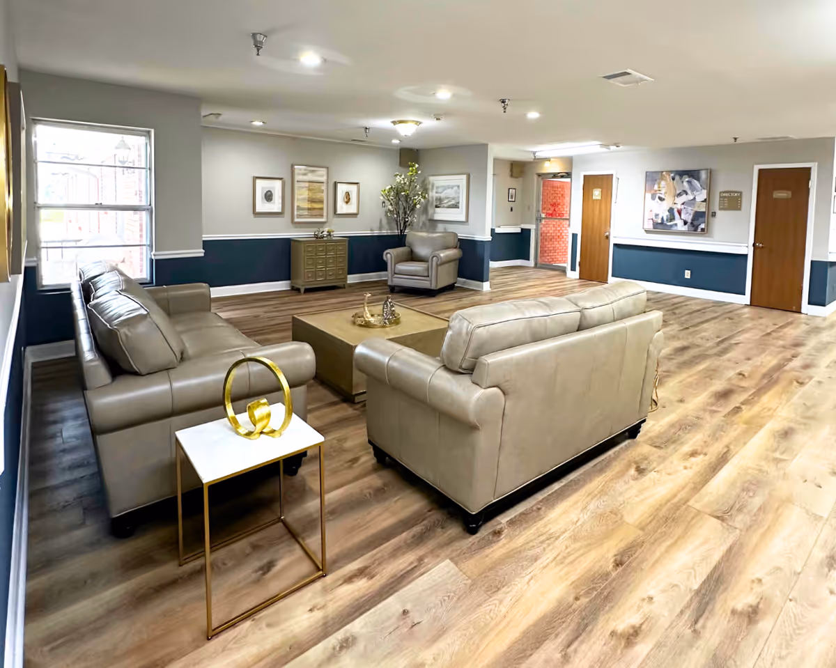 Spacious furnished common lounge with beige leather sofas, a central coffee table, and wood-look flooring.