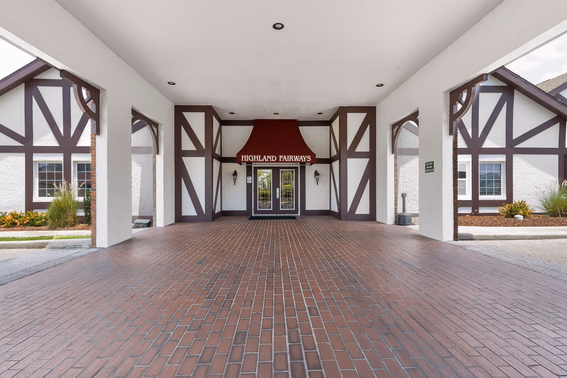Covered brick driveway leads to Highland Fairways entrance with Tudor-style exterior and signage.