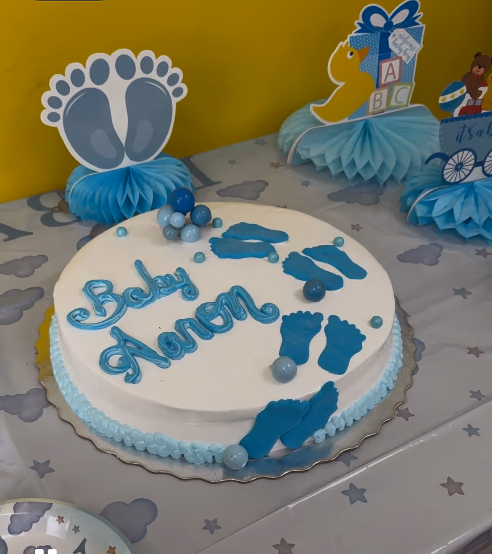 White cake with blue footprints and Baby Shower inscription on a decorated table.