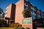 Brick senior living building with Sterling Place sign and palm trees against a blue sky.