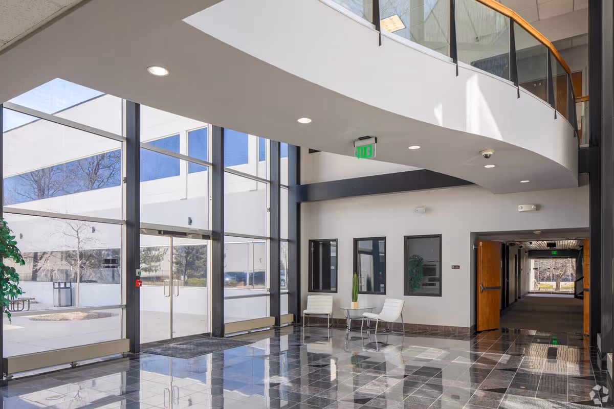 Modern facility lobby with large glass windows, tiled floor, curved balcony, and white seating.