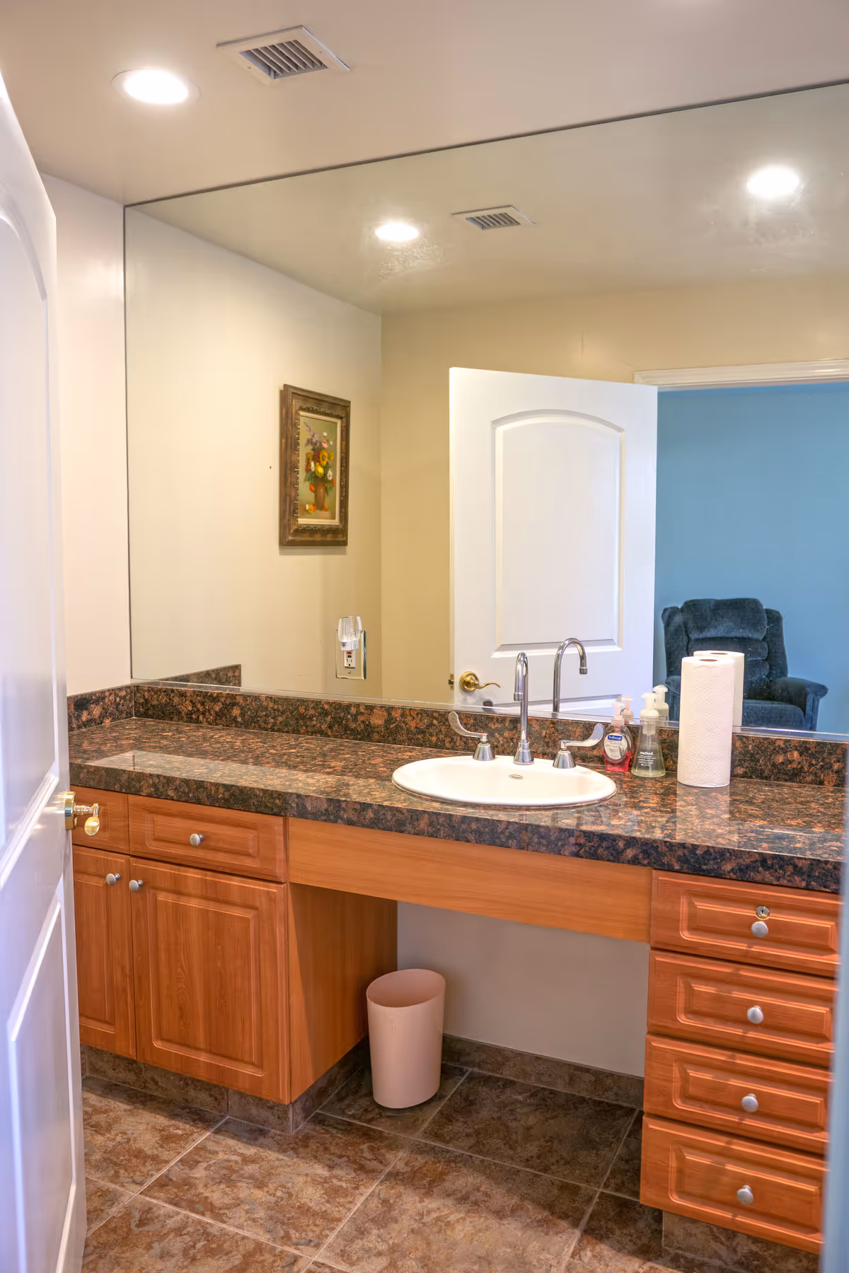 The bathroom vanity features a sink, mirror, and wood cabinets in a senior living facility.