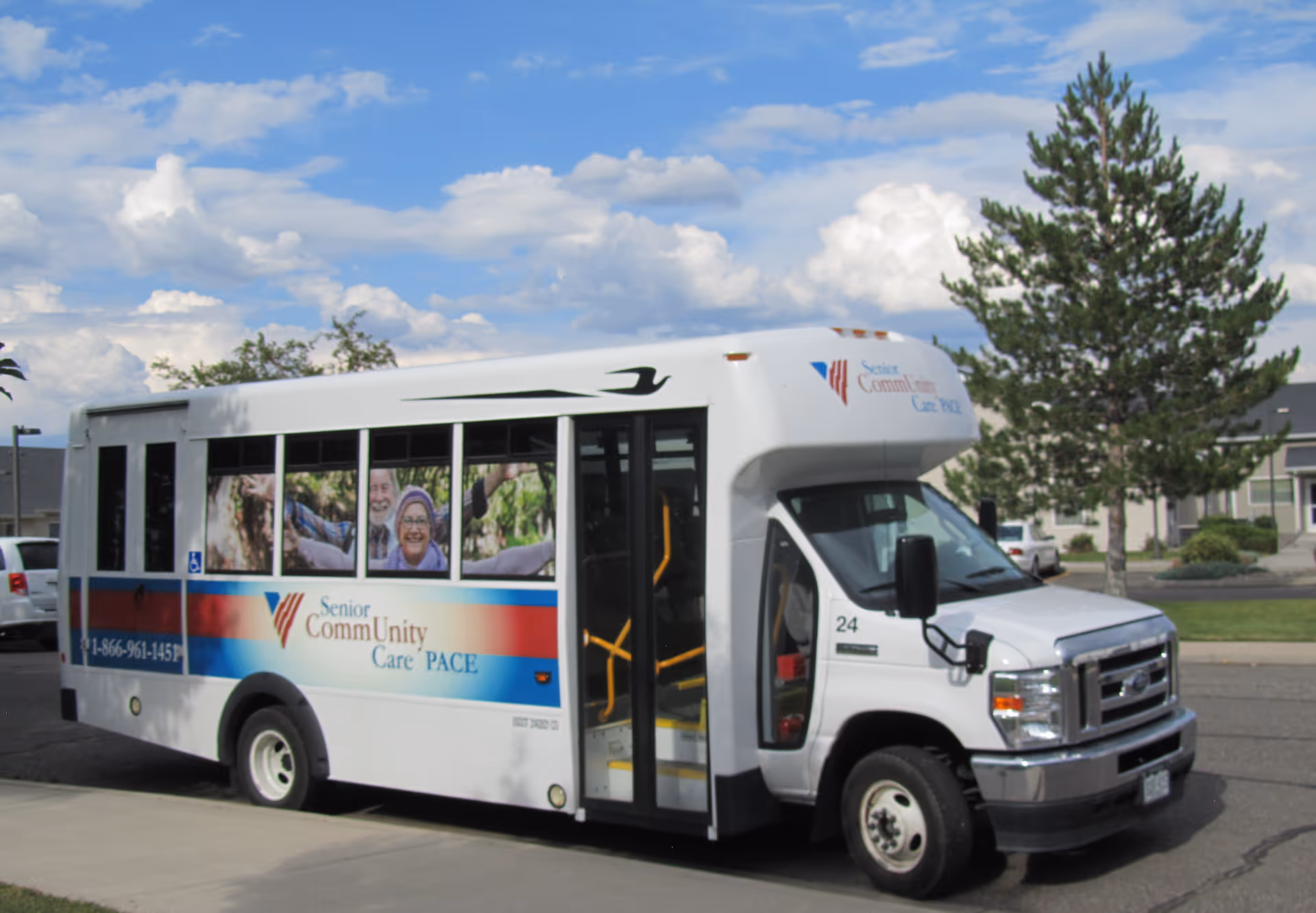White Senior CommUnity Care PACE bus parked in a lot with trees.