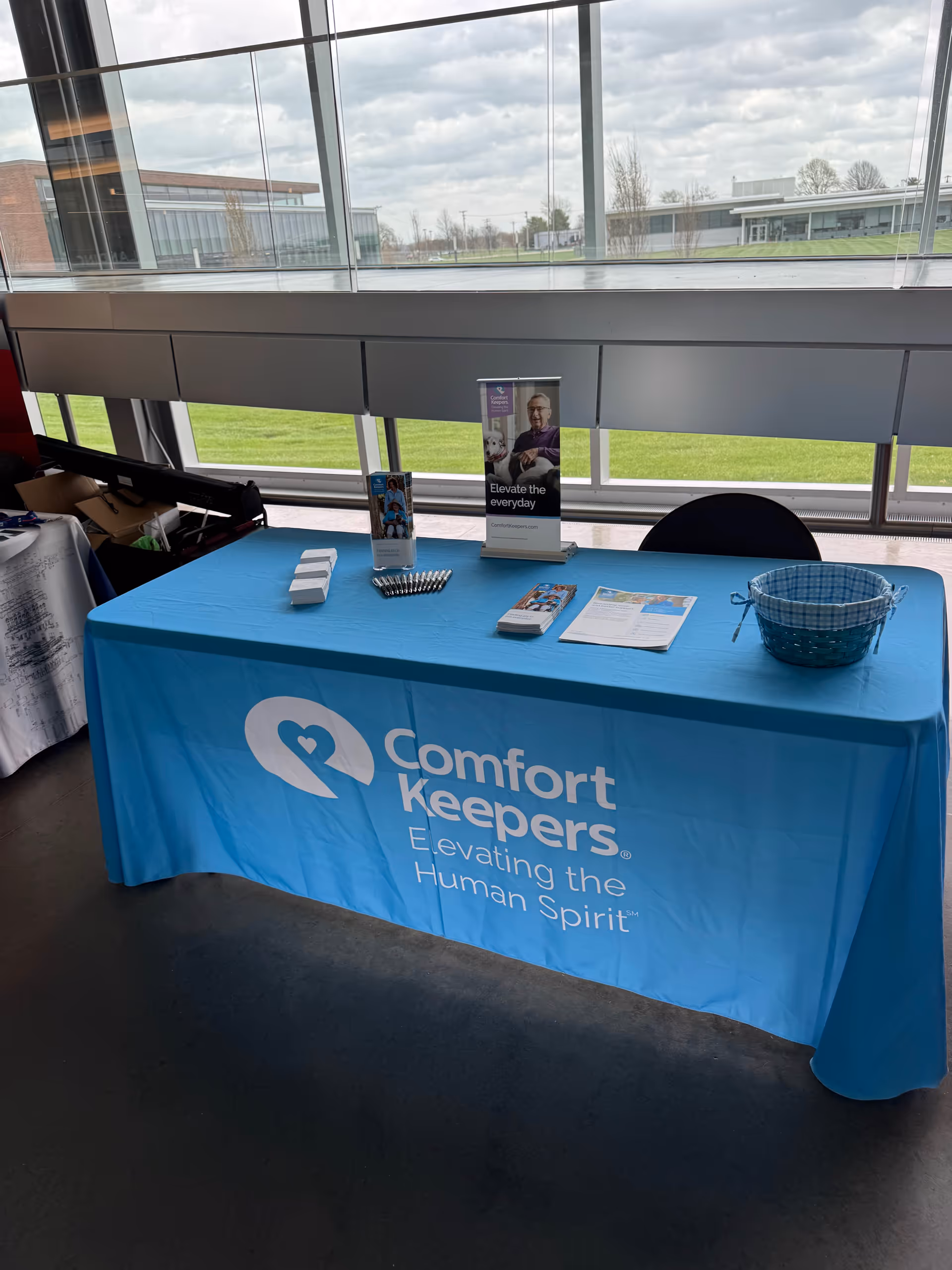 Blue Comfort Keepers table with brochures inside a bright indoor lobby.