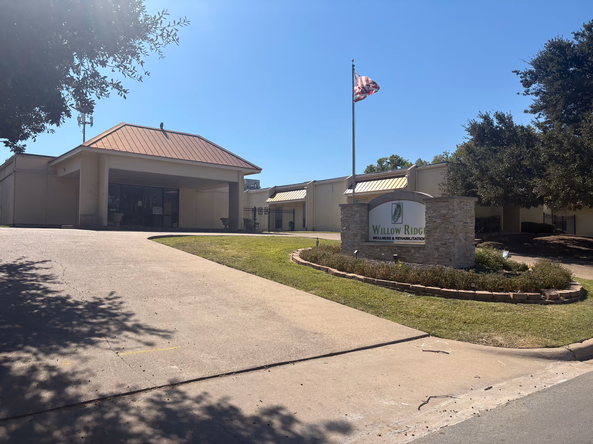 Exterior view of a single-story senior living facility with entrance, flagpole, and sign.