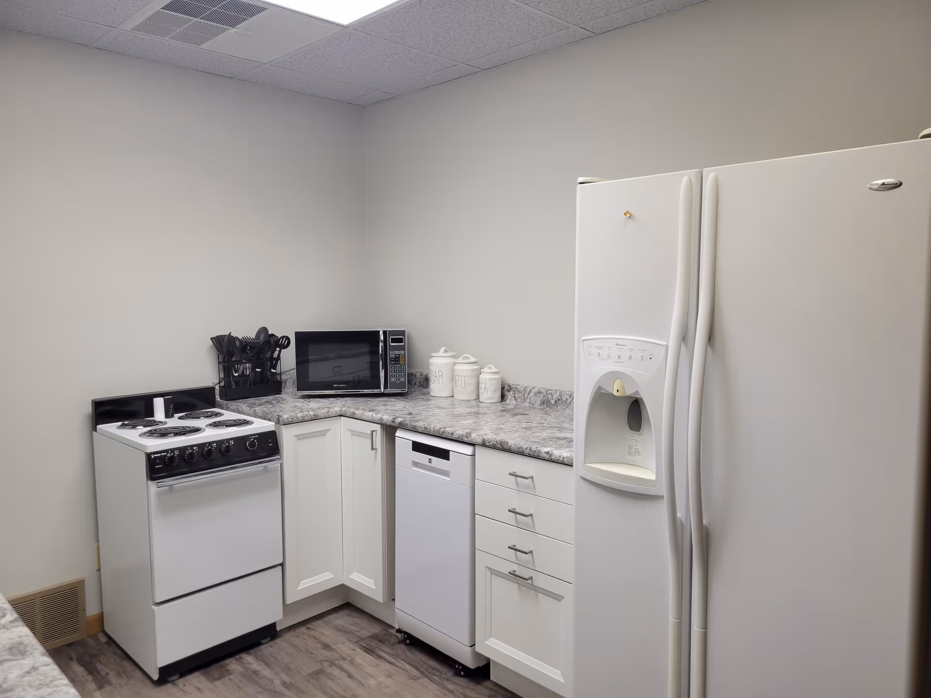 Compact kitchen with stove, refrigerator, microwave, dishwasher, and white cabinets.