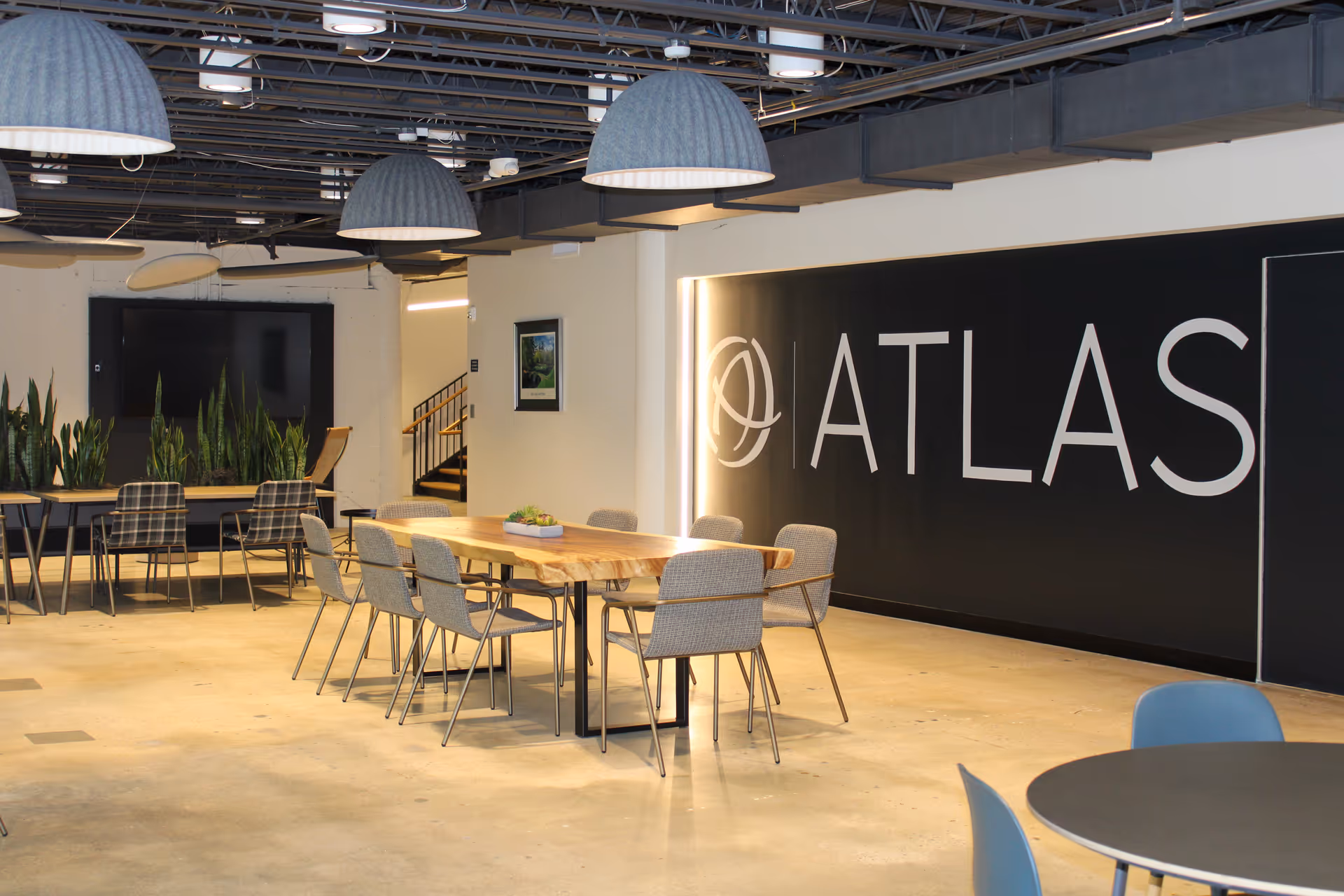 Modern indoor communal space with long wooden table, chairs, and an Atlas sign