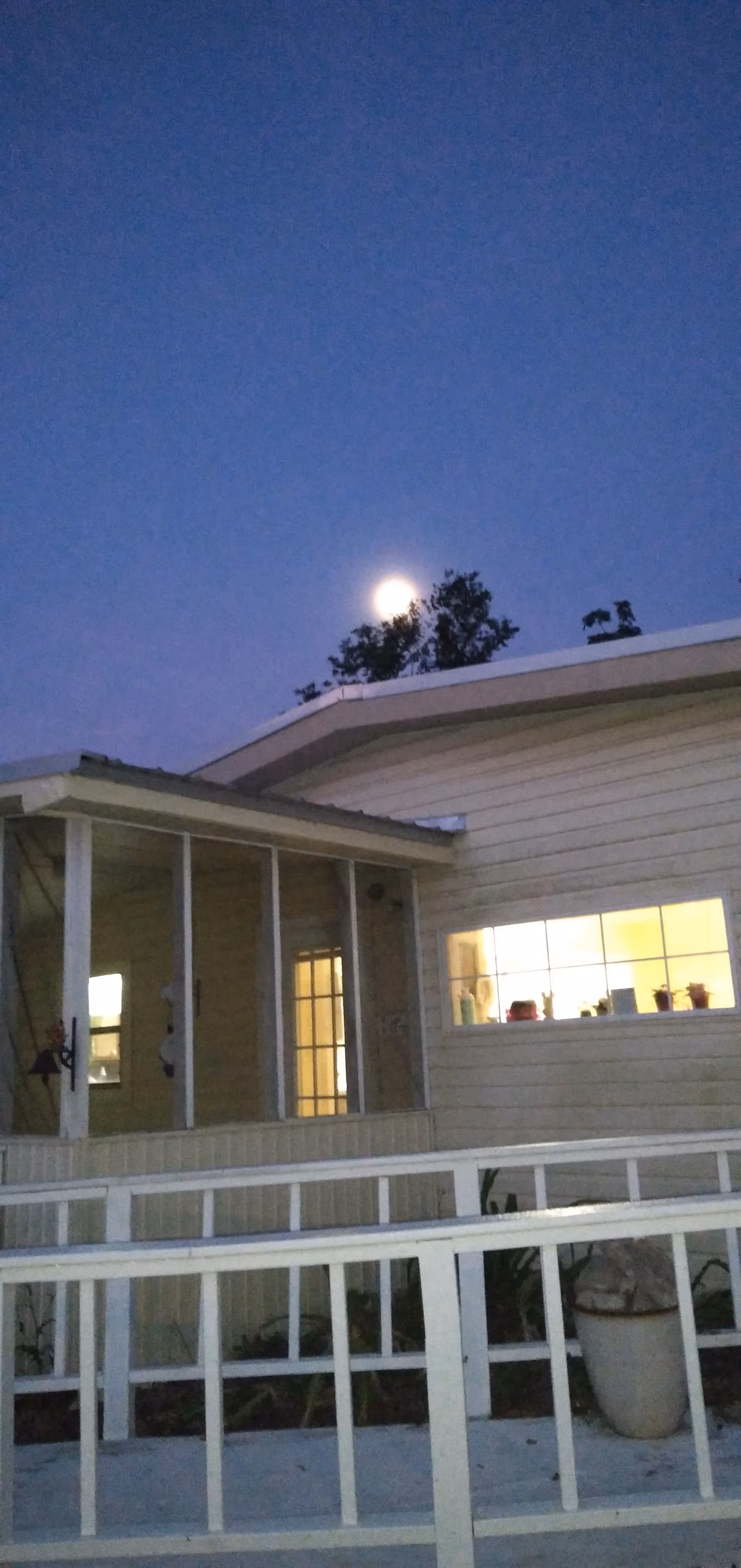 Evening exterior of a light-colored residential facility with a covered porch and railing.