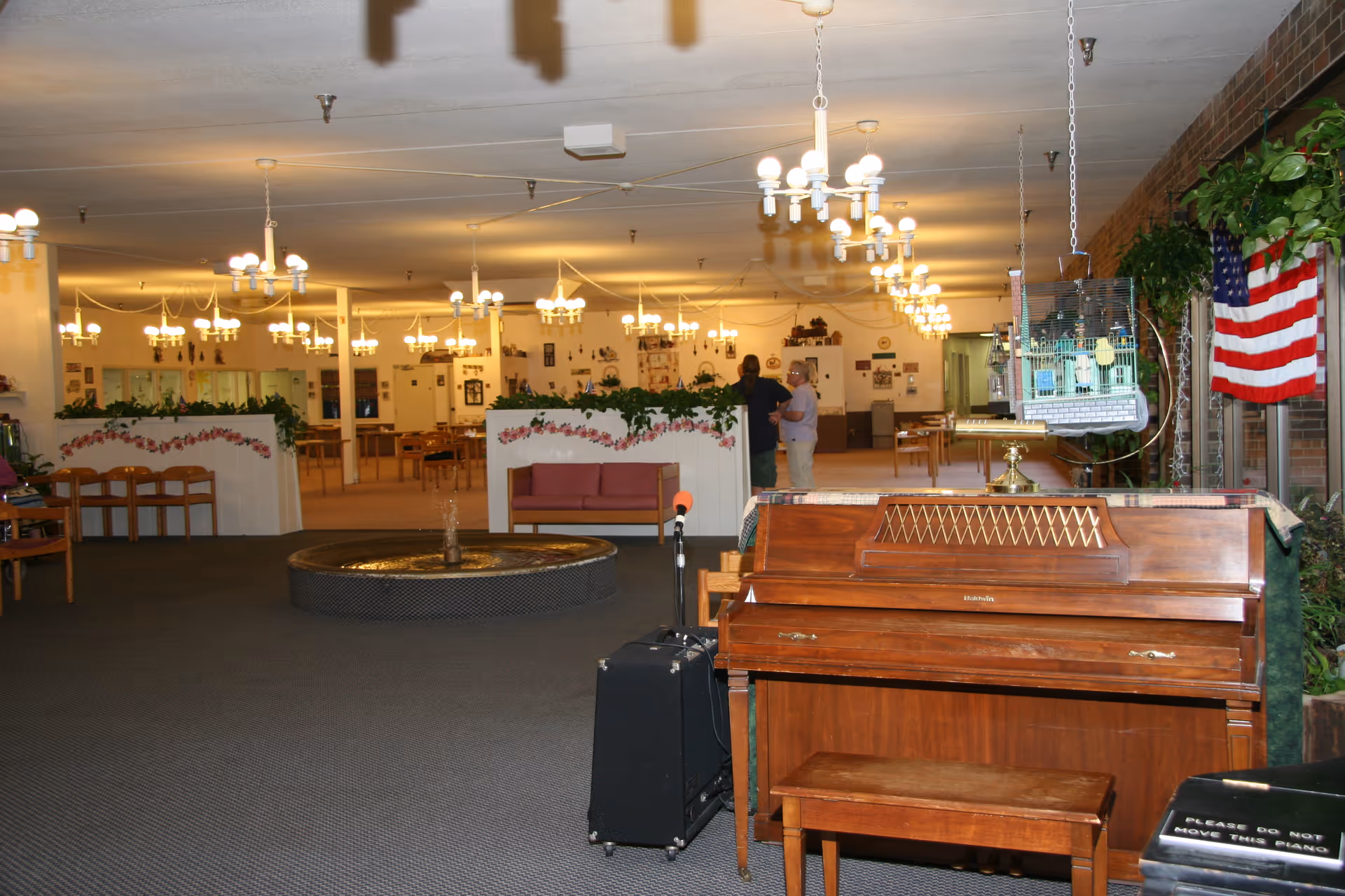 Interior common area of Pine Acres with a piano, fountain, seating, and chandeliers.