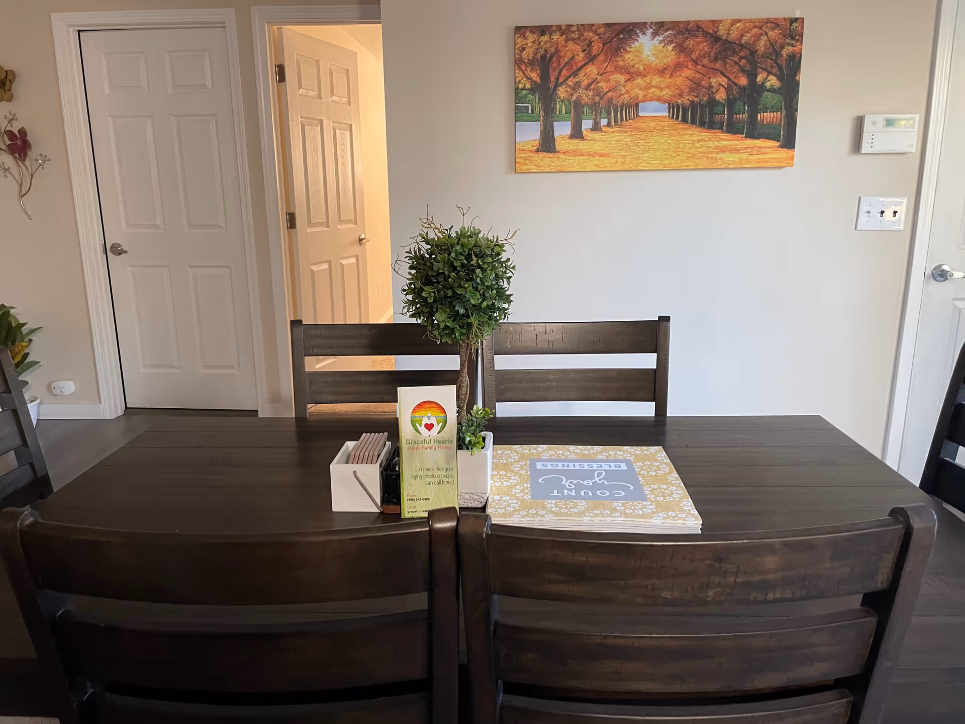 Dining area with a dark wooden table, chairs, plant centerpiece, and wall art.