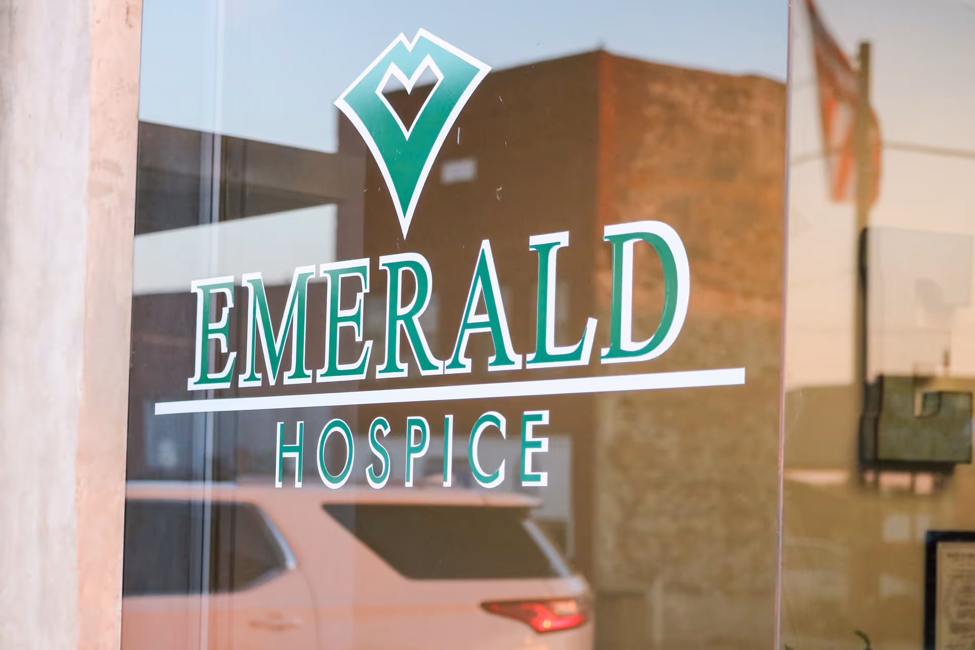 Glass storefront door shows Emerald Hospice branding with a green logo and reflections.