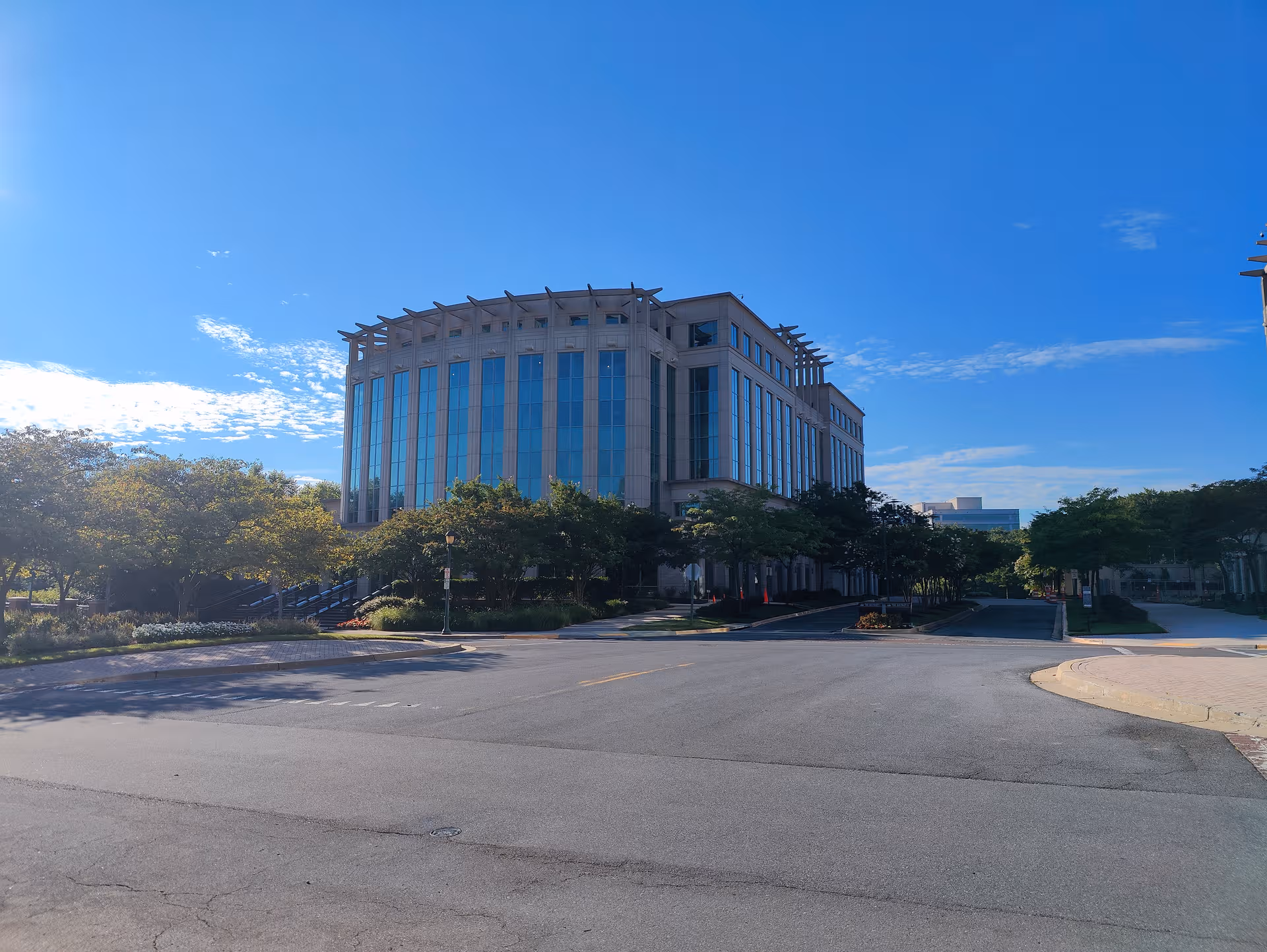 Exterior view of a modern multi-story glass building with trees and a street.