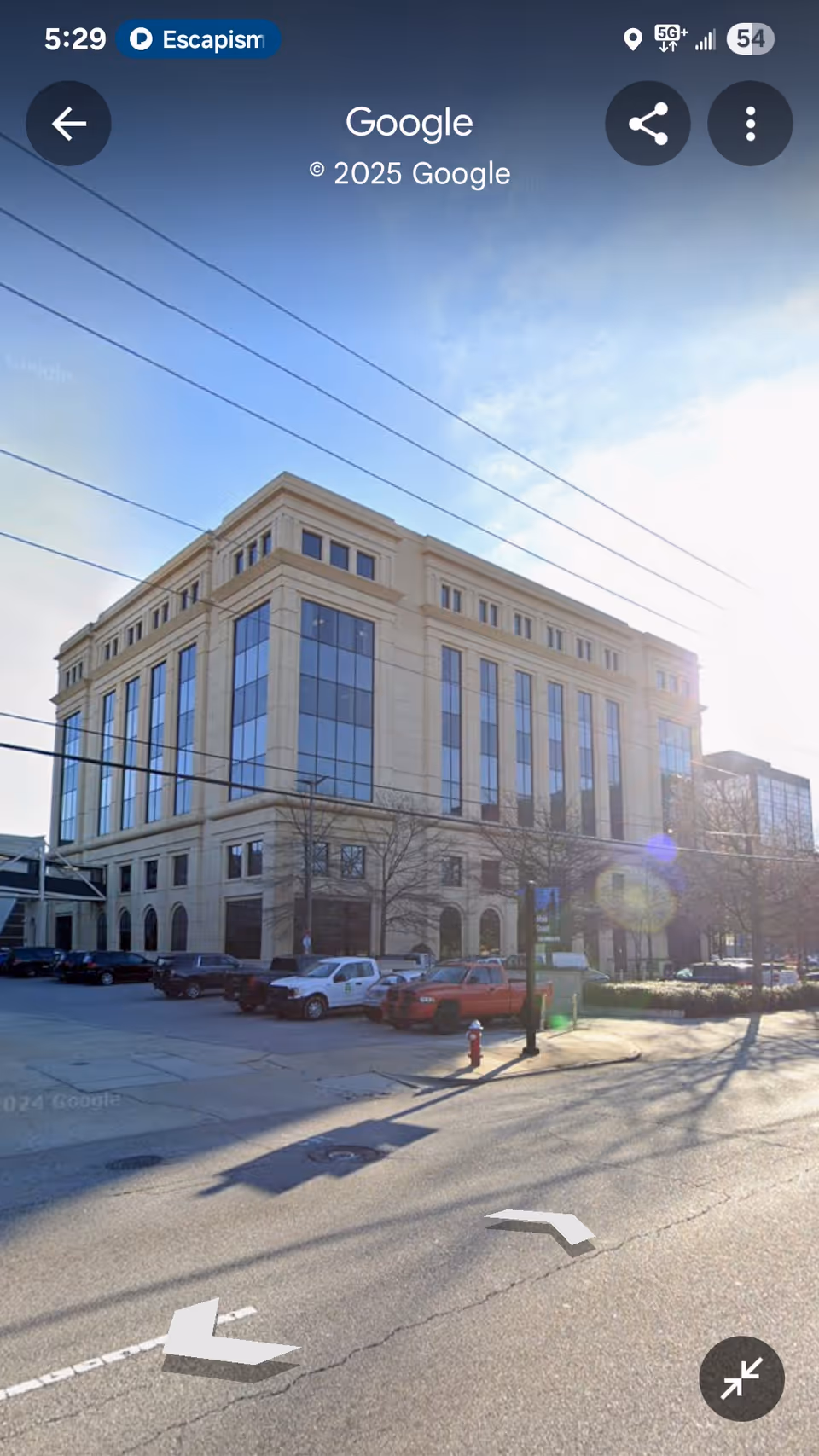 Tall beige building with glass windows along a sunlit street and parked cars.