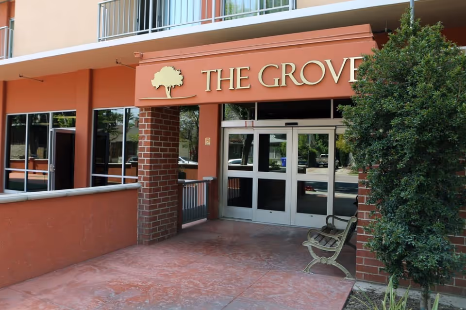 Exterior entrance of The Grove Care and Wellness building with glass doors and bench.