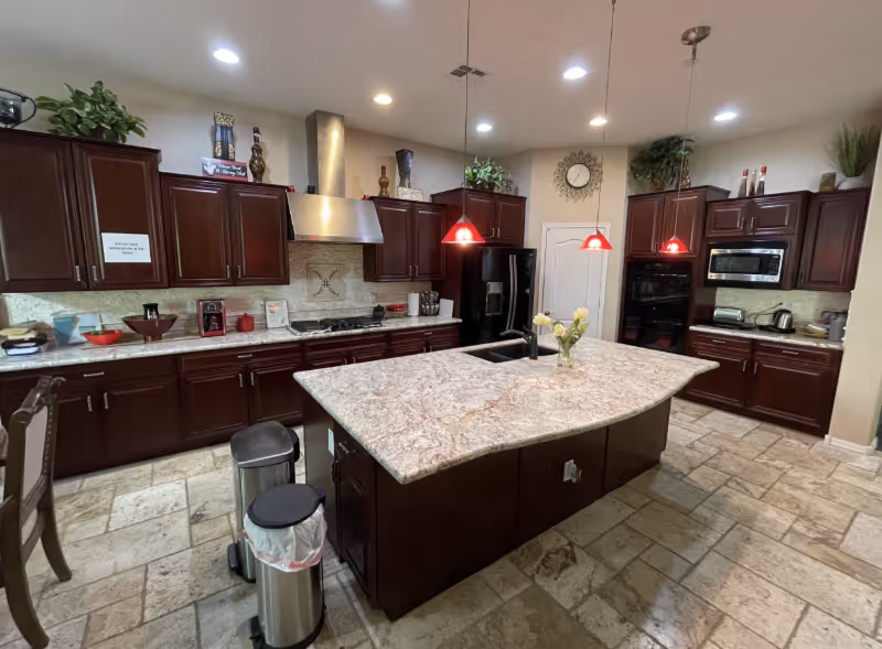 Large dark wood kitchen with island, stainless appliances, and pendant lights in Destiny Care Home.