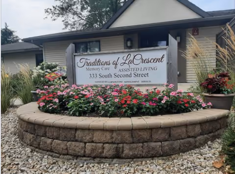 Exterior view of Traditions of La Crescent sign surrounded by a circular brick planter with flowers.