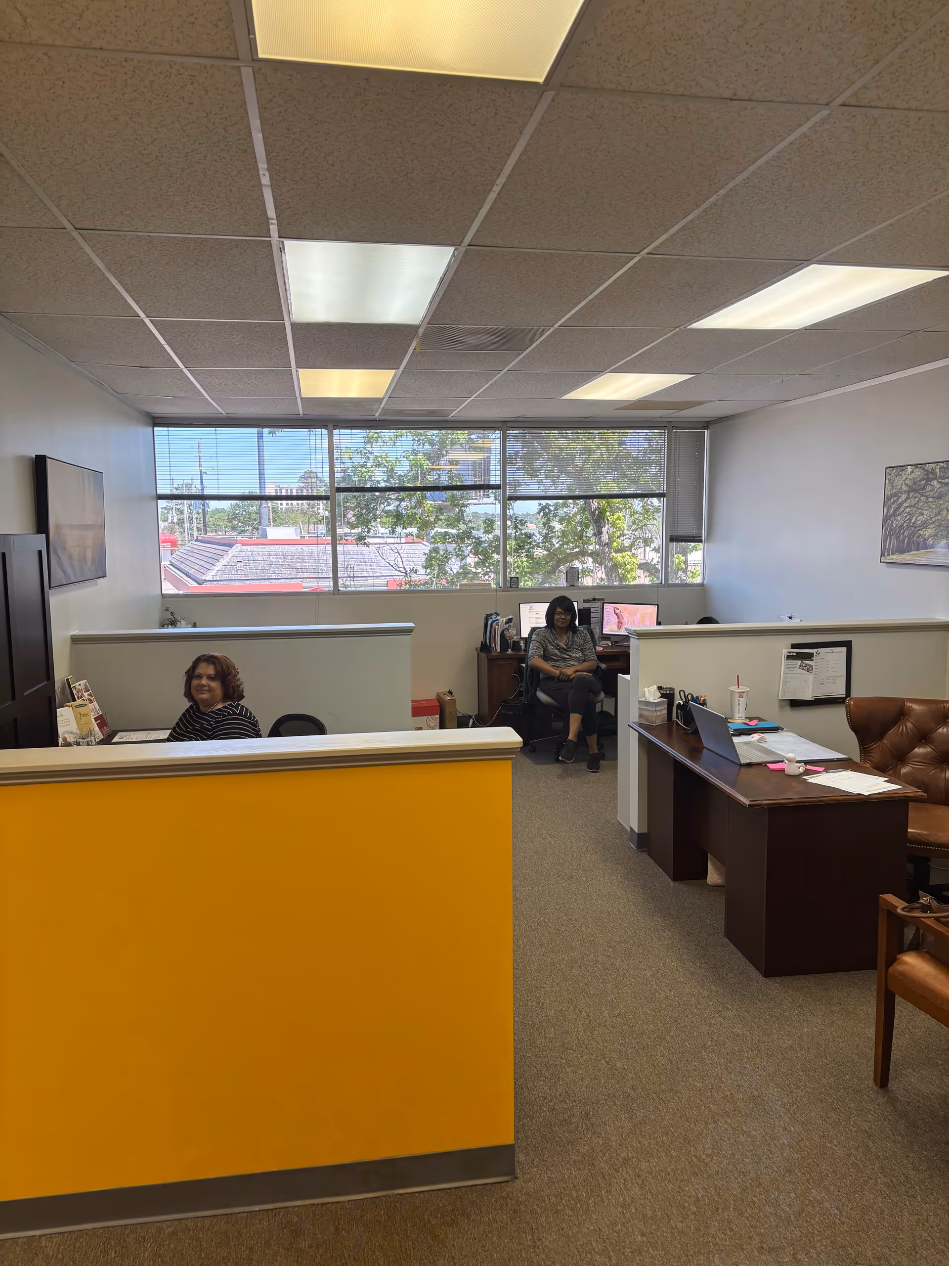 Senior living facility reception area with two staff members seated near cubicles by windows