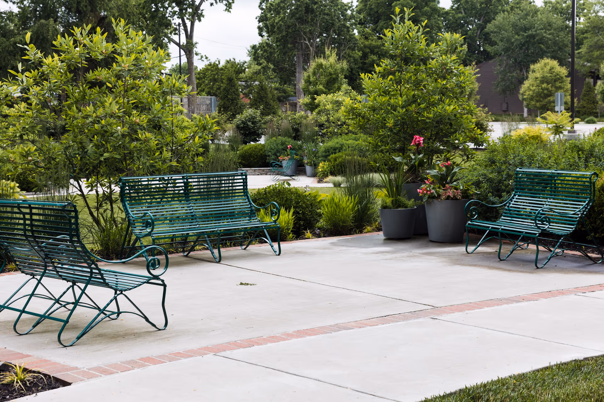 An outdoor courtyard features green metal benches, potted plants, and trees.