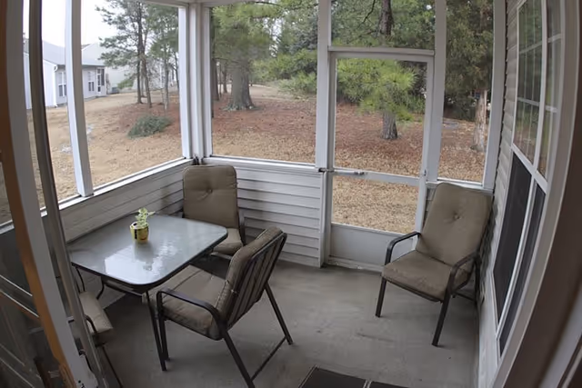 Screened outdoor porch with a glass table and cushioned chairs overlooking a yard.